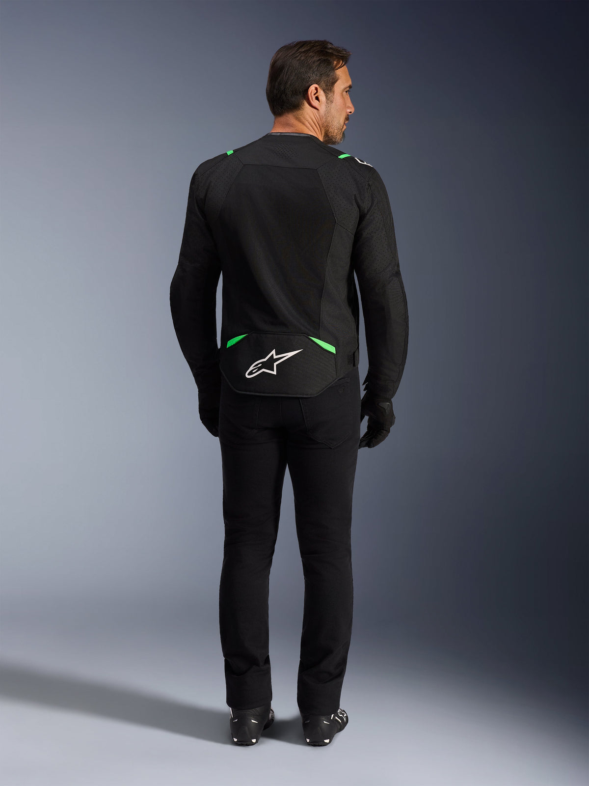 Alpinestars T-SPS Air V2 Jacke, Motorradjacke, Schwarz und Fluo-Grün, Rückansicht mit weißem Logo am unteren Rücken, getragen mit passender schwarzer Hose und Stiefeln, belüftetes Mesh-Design für sportliches Fahren