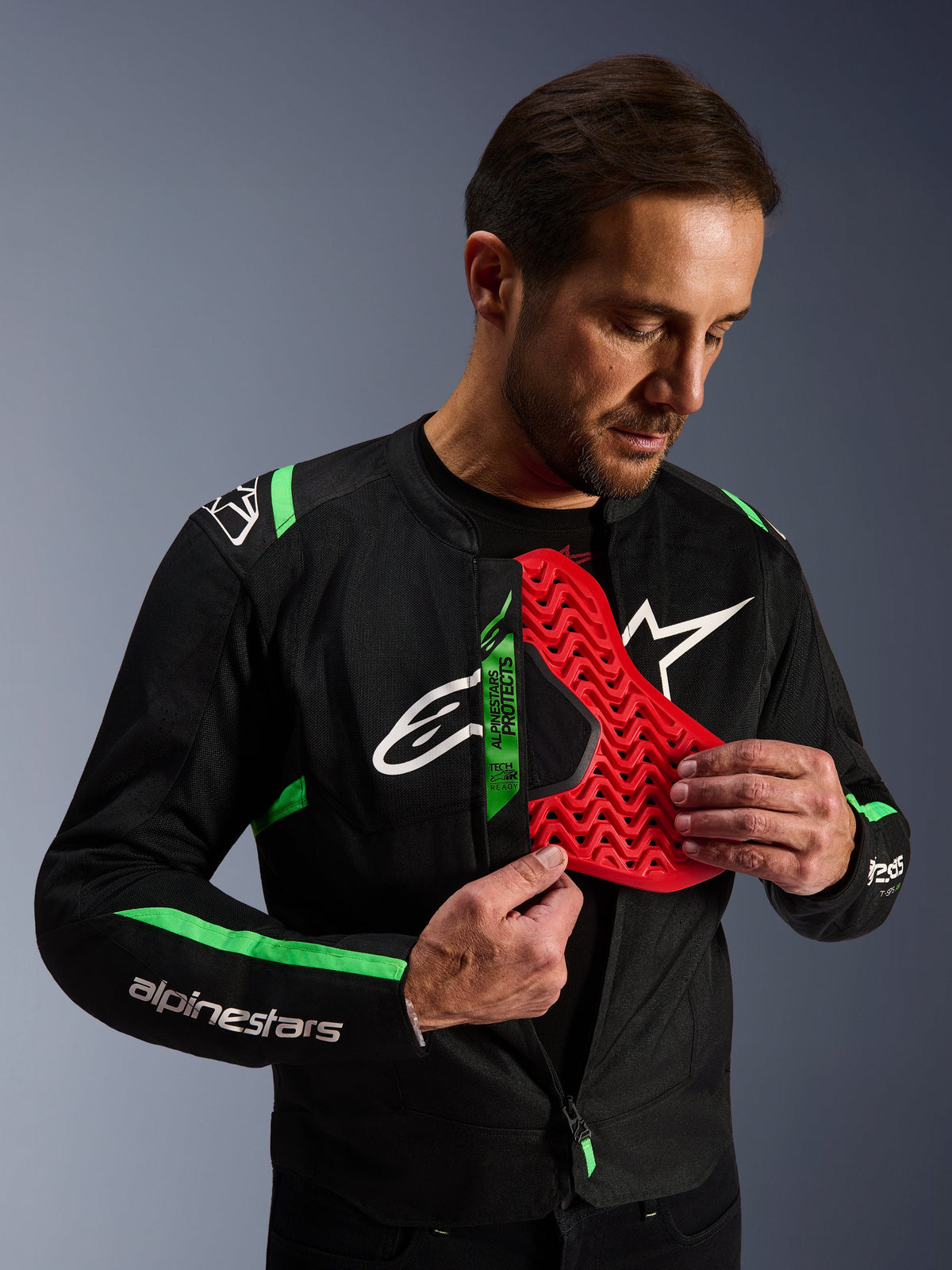 Alpinestars T-SPS Air V2 Jacke, Motorradjacke in Schwarz Fluo-Grün, Mann präsentiert einen roten Nucleon Brustprotektor-Einsatz, Tech-Air Ready Label, sportliches Textildesign mit Mesh-Einsätzen