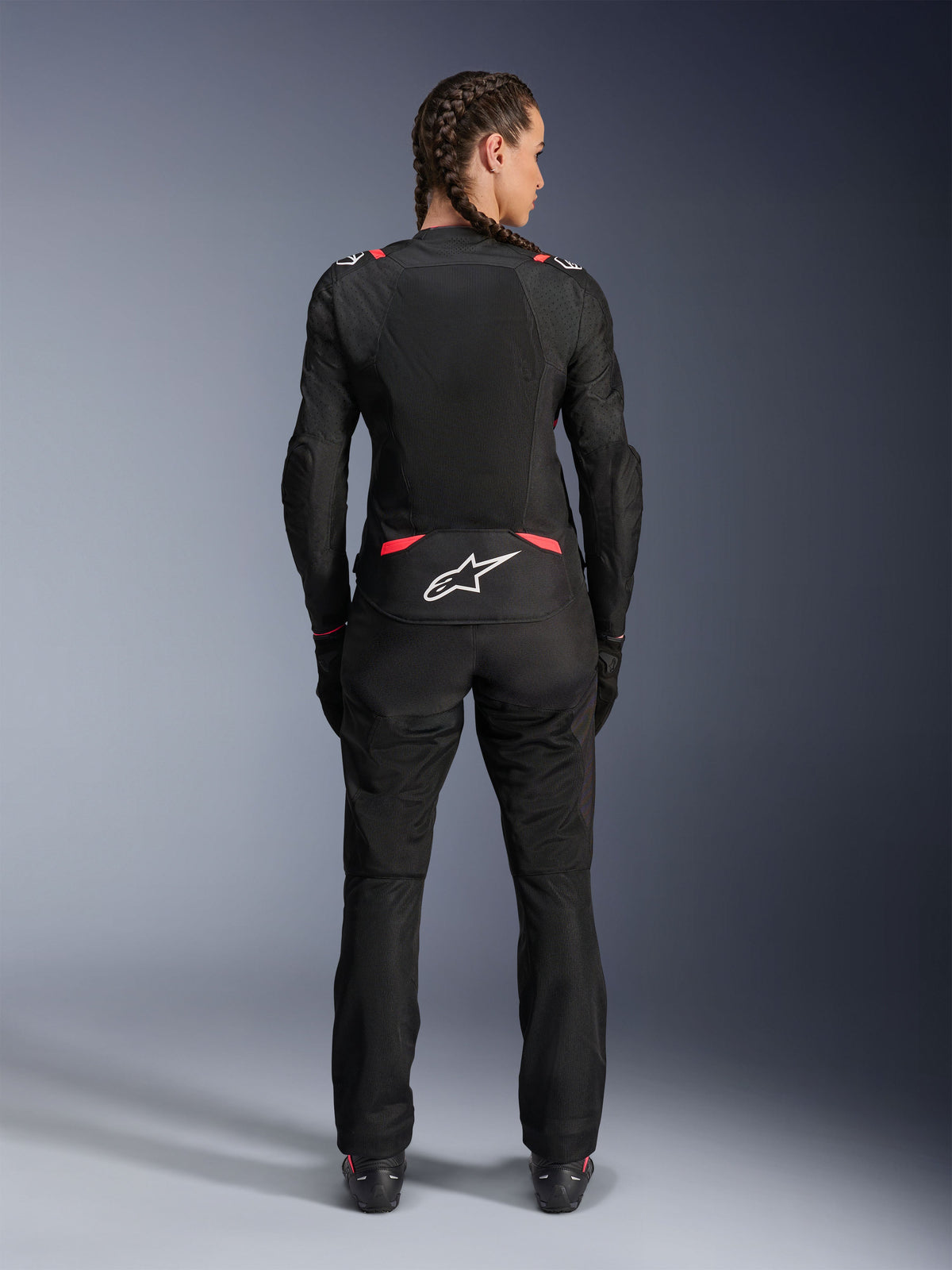 Alpinestars Stella T-SPS Air V2 Jacke, Damen-Textilmotorradjacke, Schwarz und Diva Pink, Rückansicht an einem Modell mit geflochtenem Haar, mit großen Mesh-Paneelen zur Belüftung, weißes Astars-Logo am unteren Rücken, kombiniert mit passender schwarzer Motorradhose.