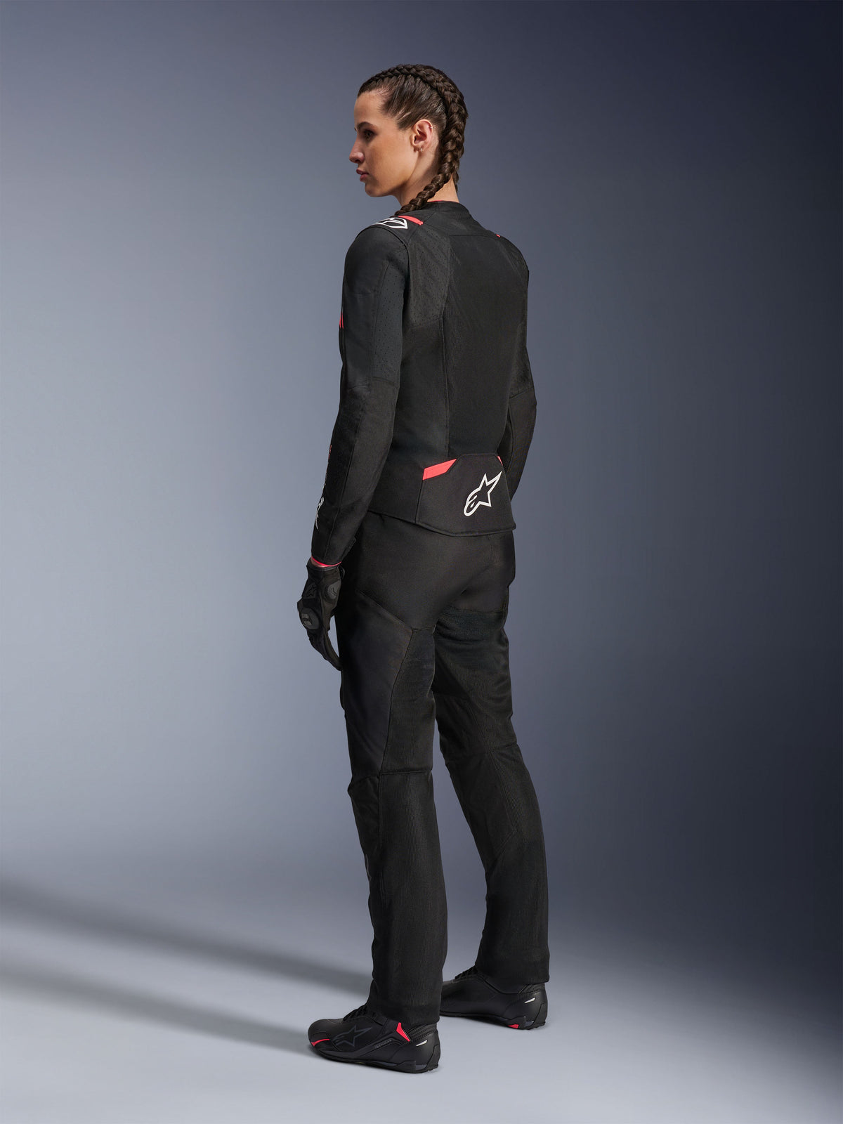 Alpinestars Stella T-Sps Air v2 Damenjacke, Schwarz und Diva Pink, Textil-Motorradjacke in der Rückansicht mit großen Mesh-Einsätzen für Luftzirkulation und weißem Stern-Logo auf dem Rücken, getragen mit passender schwarzer Fahrhose, Handschuhen und Stiefeln.