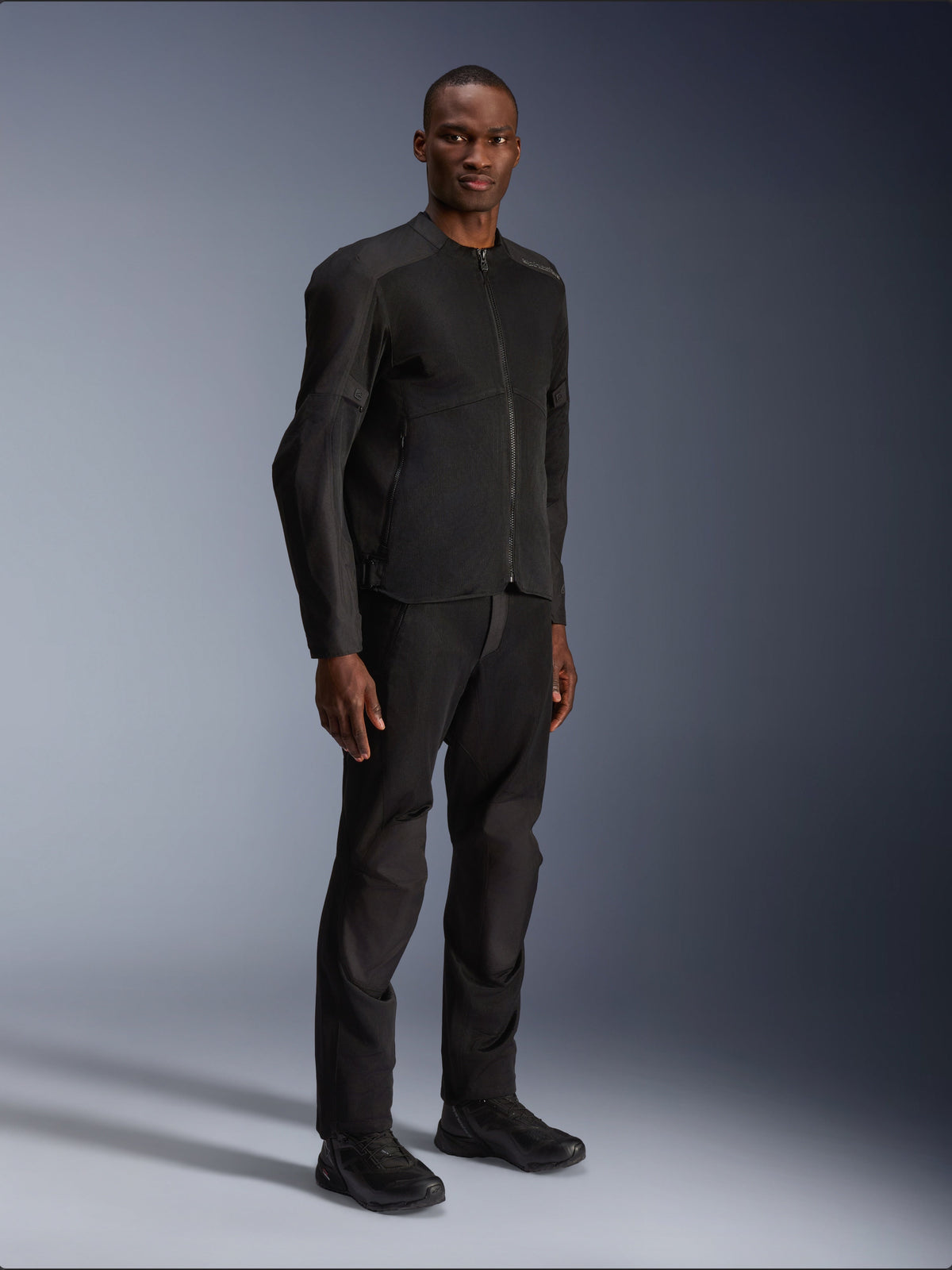 Alpinestars C-1 Air Jacke, Schwarz, getragen von einem Model mit passender schwarzer Motorradhose und Schuhen, mit großen Tech-Mesh-Einsätzen für Luftzirkulation, cleanes urbanes Design mit schmaler Passform.
