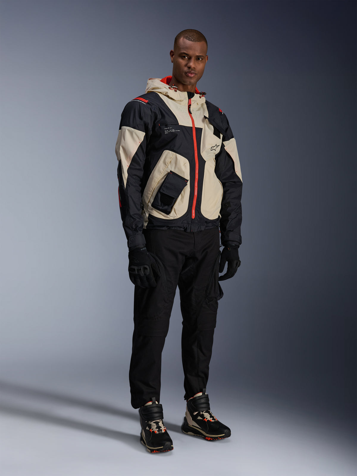 Alpinestars Acteon Hose, schwarze Motorradhose, getragen mit einer schwarz-beige-roten Mogress Air Jacke, schwarzen Motorradhandschuhen und passenden High-Top-Motorrad-Sneakern, moderne urbane Motorradausrüstung für Herren