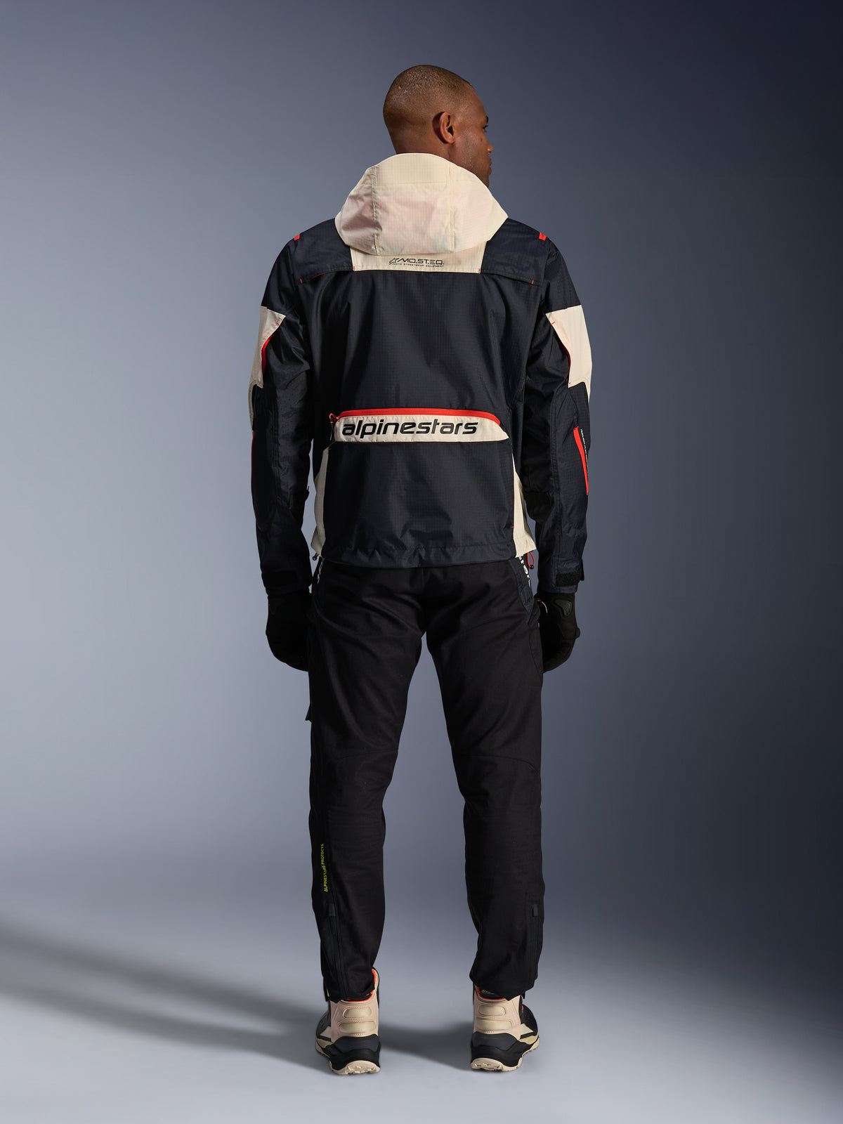 Alpinestars Mogress Air Jacke, urbane Herren-Motorradjacke, Schwarz und Orange, Rückansicht mit cremefarbener Kapuze.