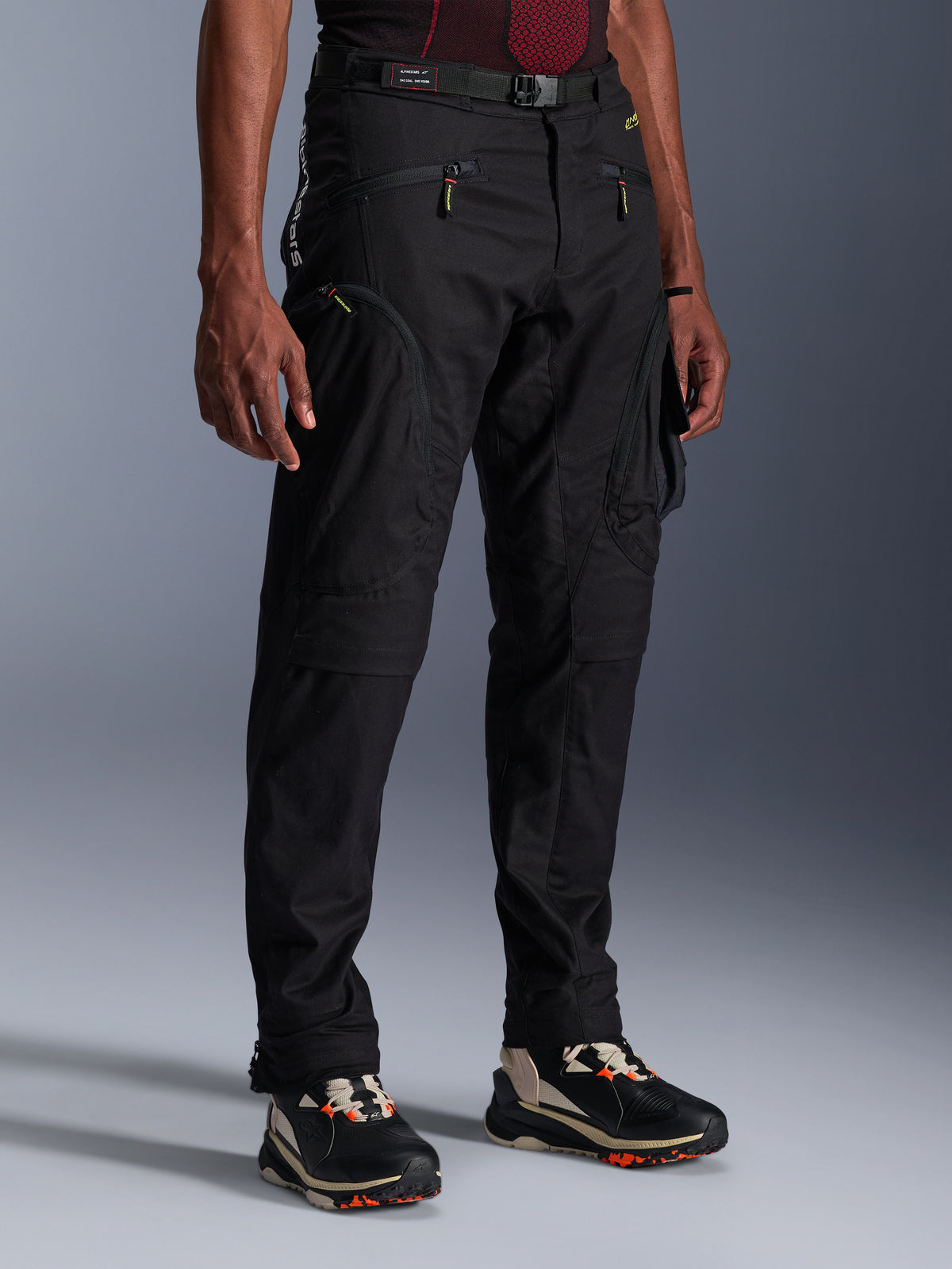 Alpinestars Acteon Hose, schwarze Motorradhose, an einem Model präsentiert, mit moderner, schmal zulaufender Silhouette, Cargo-Taschen mit Reißverschluss, verstellbarem Taillengürtel und technischen Sneakers, urbane Motorradbekleidung