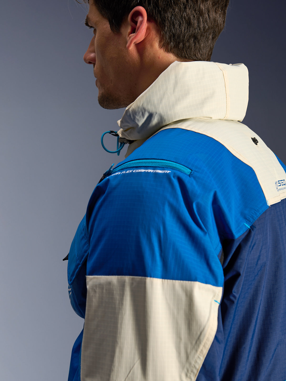 Alpinestars Mogress Air Jacke, urbane Motorradjacke für Herren, Blau und Creme, recyceltes Ripstop-Gewebe, Nahaufnahme mit hohem Kragen und Schulterprotektorenfach.