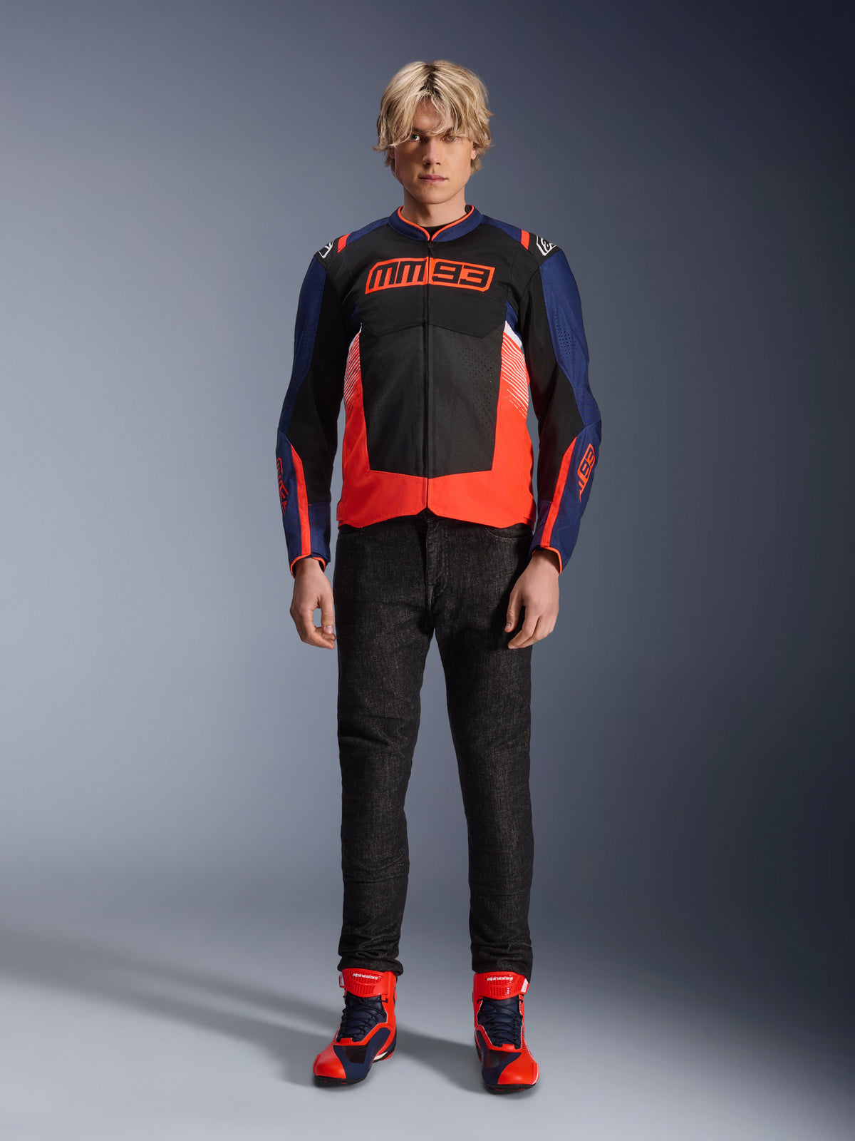 Alpinestars MM93 T-SPS Air V2 Jacket, Blue Navy and Black with Red Fluo accents, featuring the signature MM93 logo on the chest, worn with black riding pants and matching blue and red boots, urban motorcycle outfit