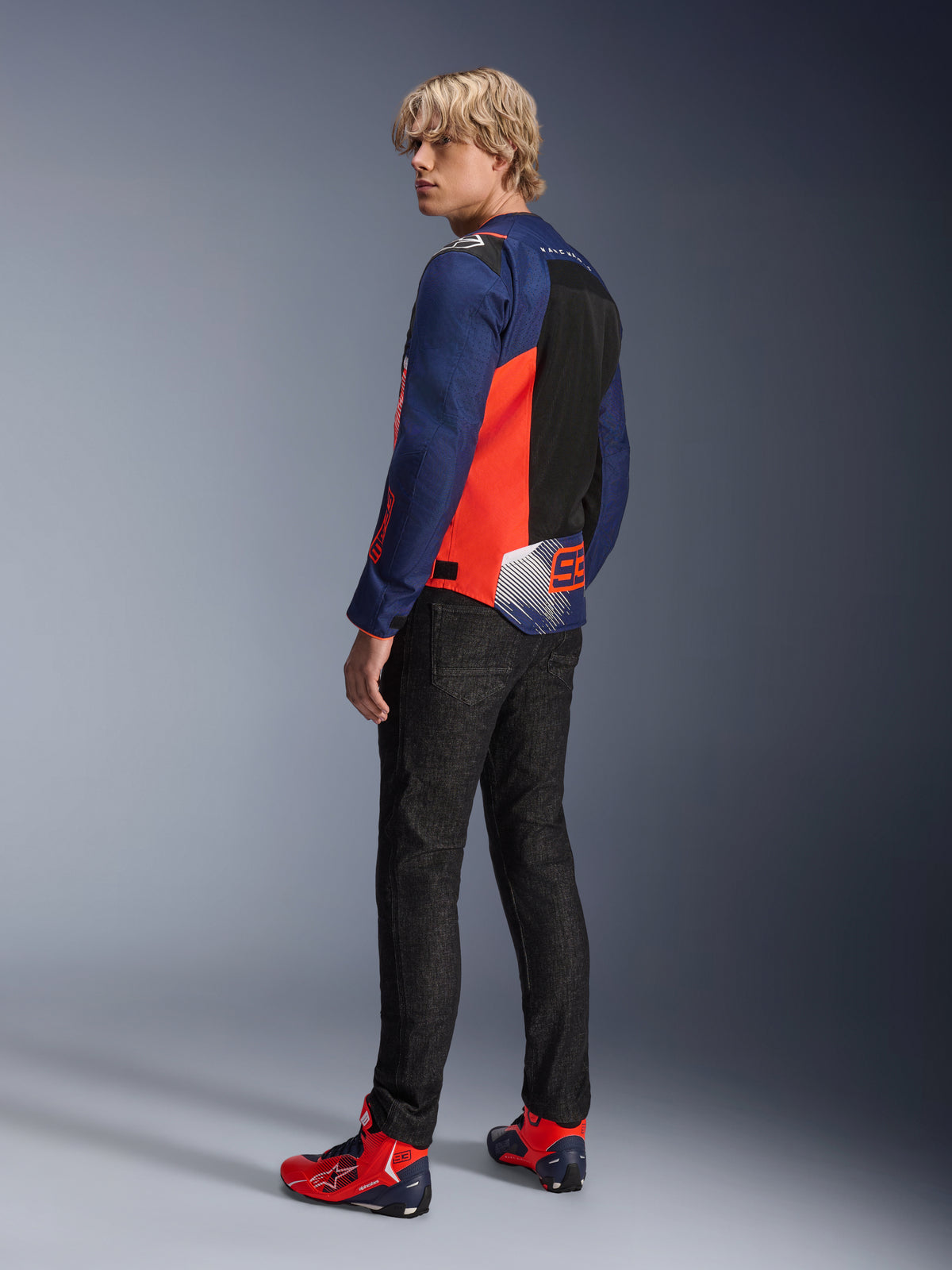 Alpinestars MM93 T-SPS Air V2 Jacket, Blue Navy and Red Fluo, worn by a model from the back with black riding jeans and matching red and blue shoes, featuring mesh panels and Marc Márquez 93 branding.