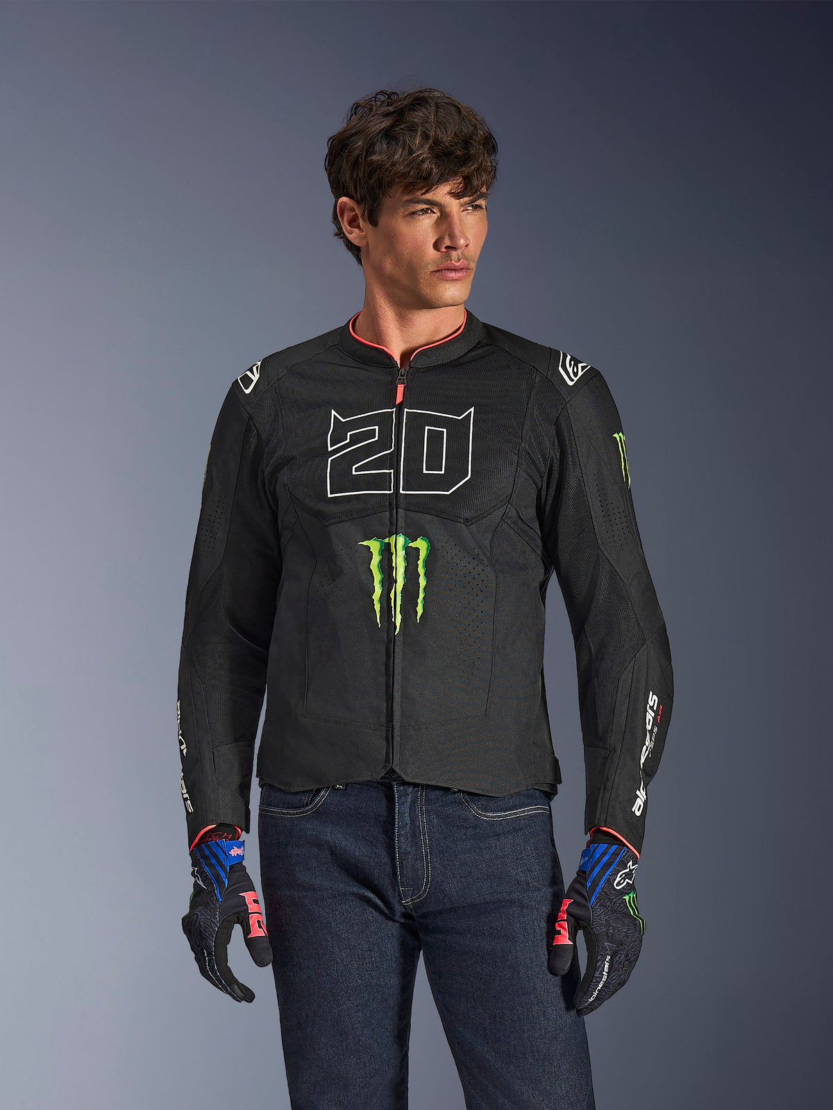 Alpinestars FQ20 T-SPS Air V2 Monster Jacke, schwarze Motorradjacke mit großer weißer '20' und grünem Monster Energy Logo, getragen von einem männlichen Model mit dunklen Jeans und passenden Handschuhen, leichte Mesh-Konstruktion für Fahrten in der Stadt
