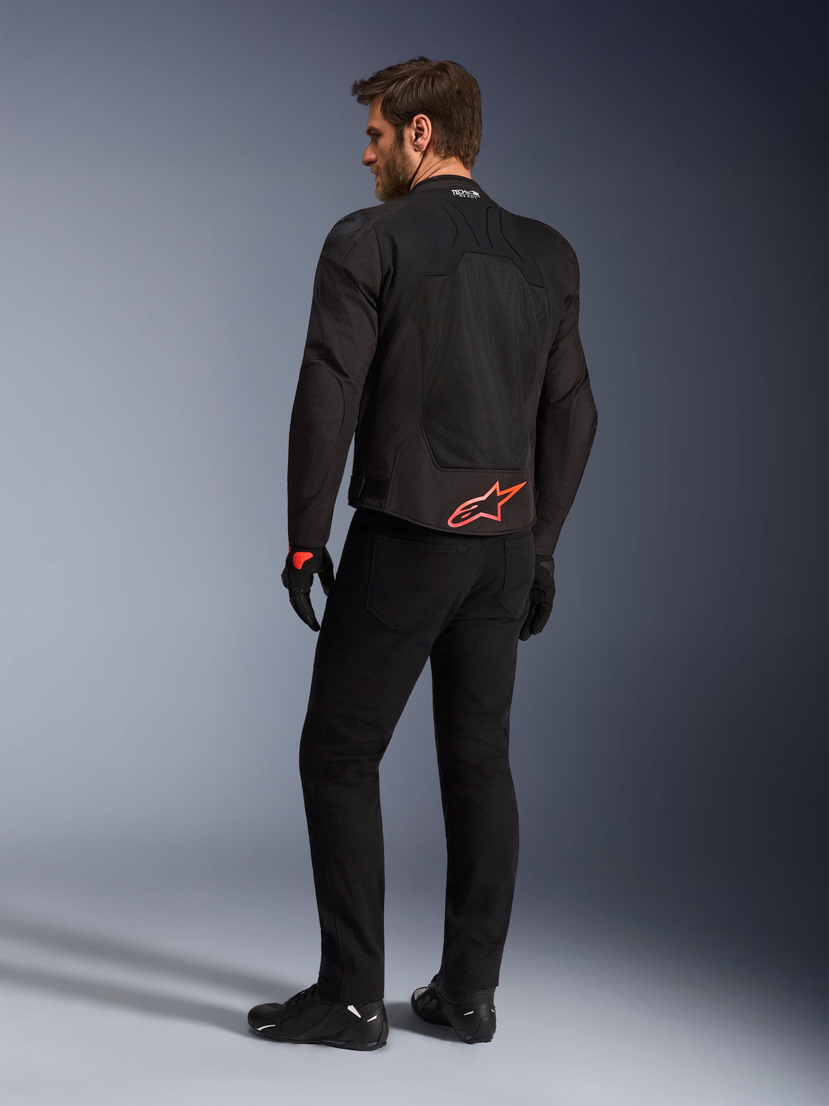 Rear view of a model wearing the Alpinestars SMX Air Jacket in Black, featuring a bright red Alpinestars logo on the lower back, 'Tech-Air Ready' branding on the collar, and technical mesh panels for ventilation, paired with black riding pants and gloves.