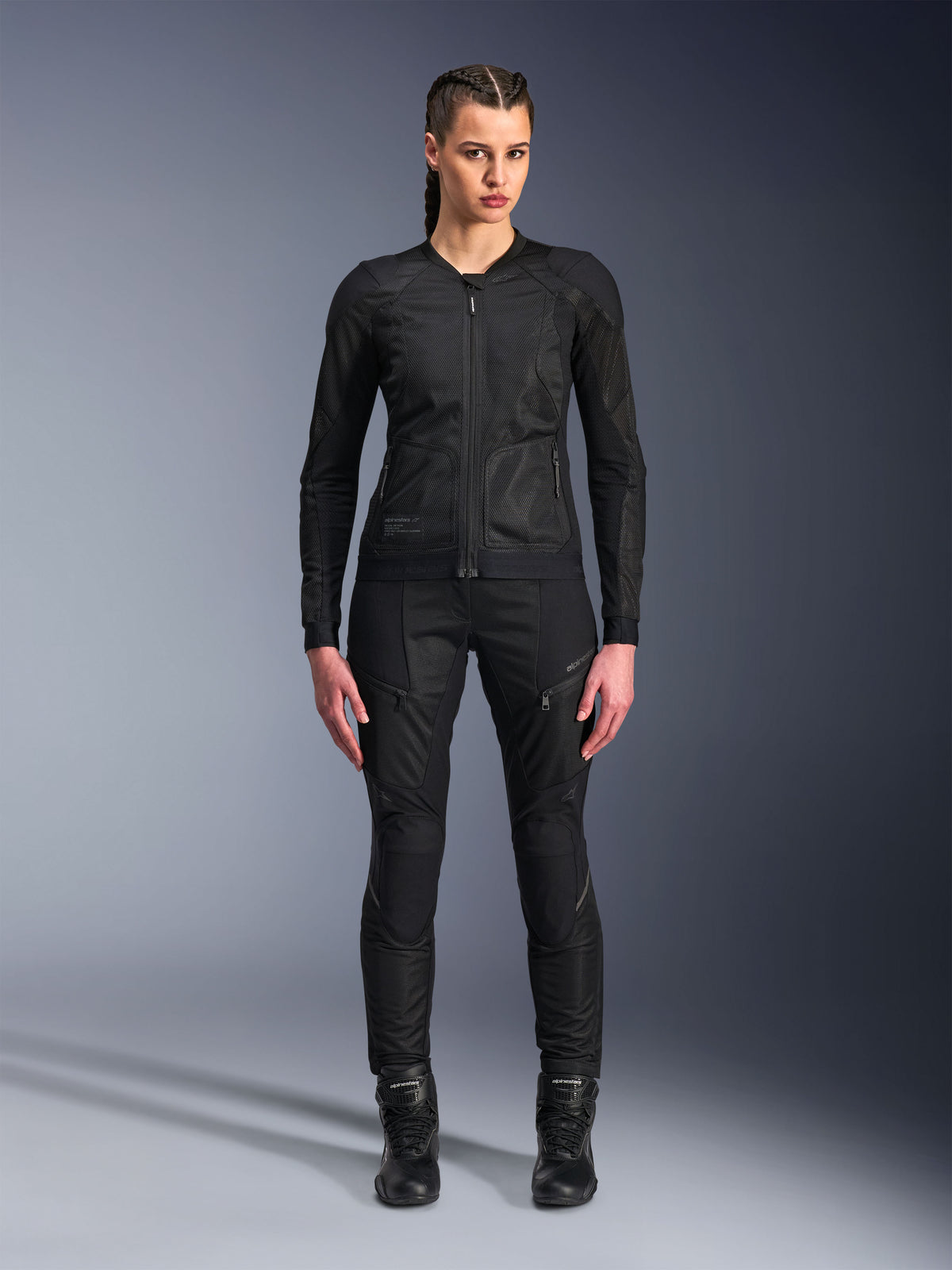 Alpinestars Stella Troop-Air Jacke, Damen-Motorradjacke, Schwarz, technische 2D-Mesh-Konstruktion mit minimalistischem Design, getragen mit schwarzer Motorradhose und Stiefeln, zeitgenössischer urbaner Motorradstil.