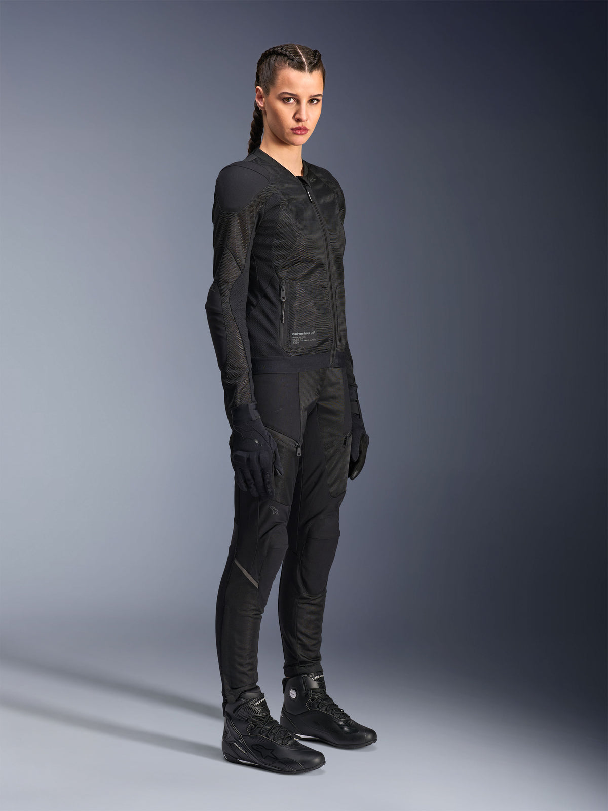 Motorradfahrerin in der Alpinestars Stella Troop-Air Jacke in Schwarz, mit technischer 2D-Mesh-Konstruktion, kombiniert mit passender schwarzer Motorradhose, Handschuhen und Stiefeln, gestylt für urbane Fahrten