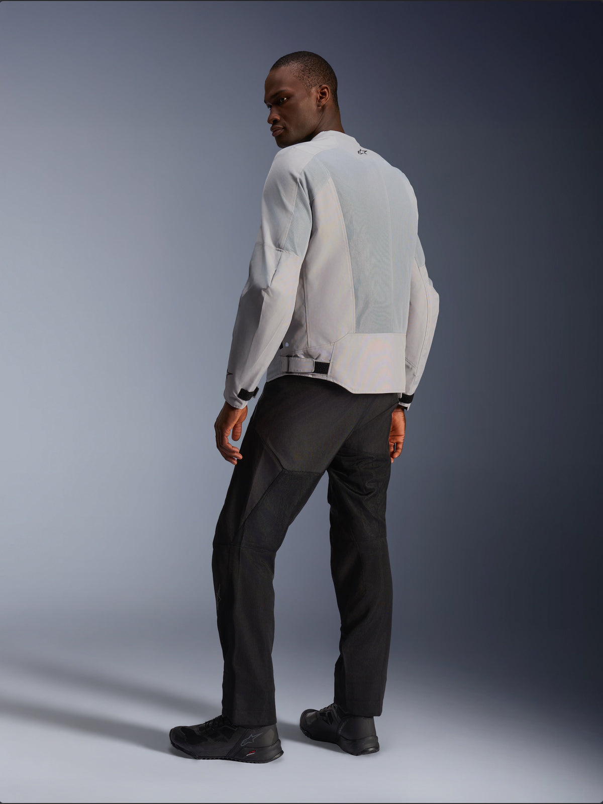 Alpinestars C-1 Air Jacke, Silber und Grau, Rückansicht an einem Modell, mit belüfteten Tech-Mesh-Einsätzen und reflektierenden Logos, getragen mit schwarzer Hose und Schuhen, urbane zeitgemäße Motorradausrüstung