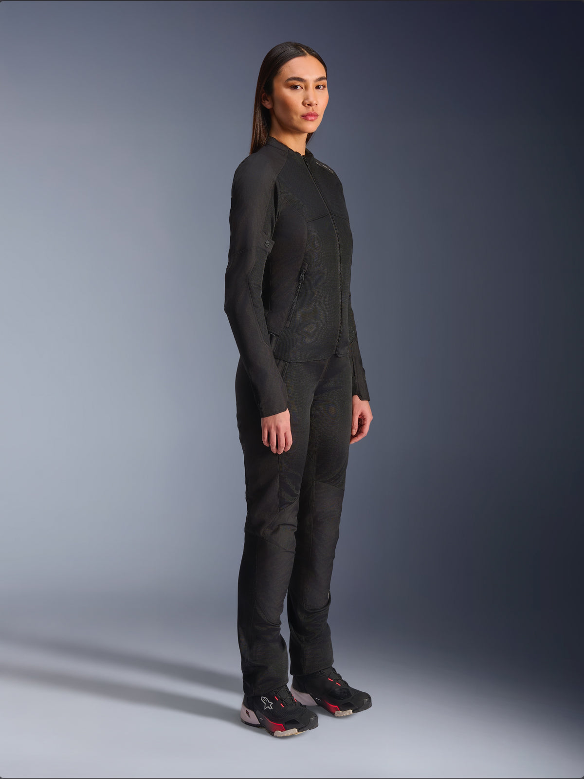 Alpinestars Woman Stella C-1 Air Jacket in Black, textile motorcycle jacket with mesh panels, worn with matching black riding pants and technical sneakers, studio shot showing a full-length urban riding outfit.