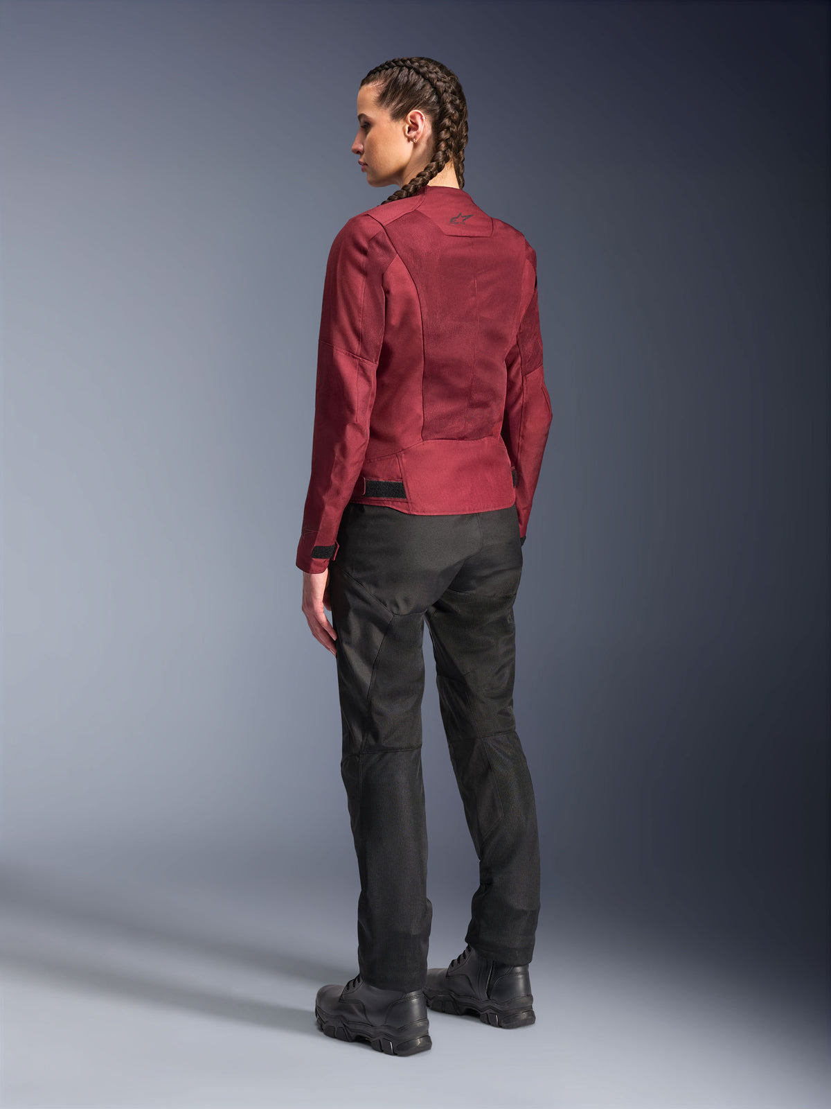 Alpinestars Stella C-1 Air Damenjacke, Burgunderrot, Rückansicht mit Mesh-Einsätzen und raffinierten Details, getragen mit schwarzer Motorradhose und Stiefeln, urbane zeitgenössische Motorradausrüstung.