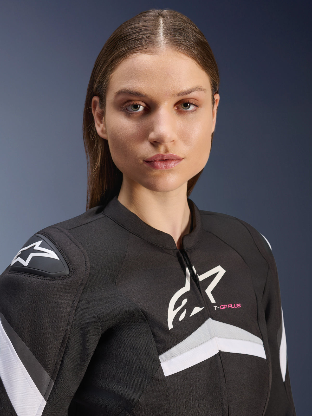 Alpinestars Stella T-GP Plus R V4 Jacket, Women's Textile Motorcycle Jacket, Black and White with grey accents and pink 'T-GP PLUS' text, close-up view of female model wearing the sport-fit jacket with white Astars logos