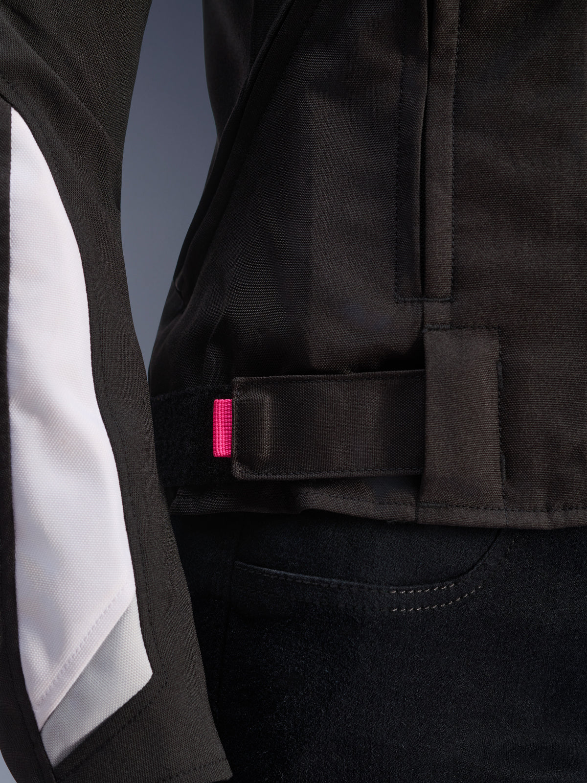 Alpinestars Stella T-GP Plus R V4 Jacket, Black and White, close-up of the adjustable waist strap with pink accent tab, durable textile construction with white sleeve paneling, sport-fit women's motorcycle jacket.
