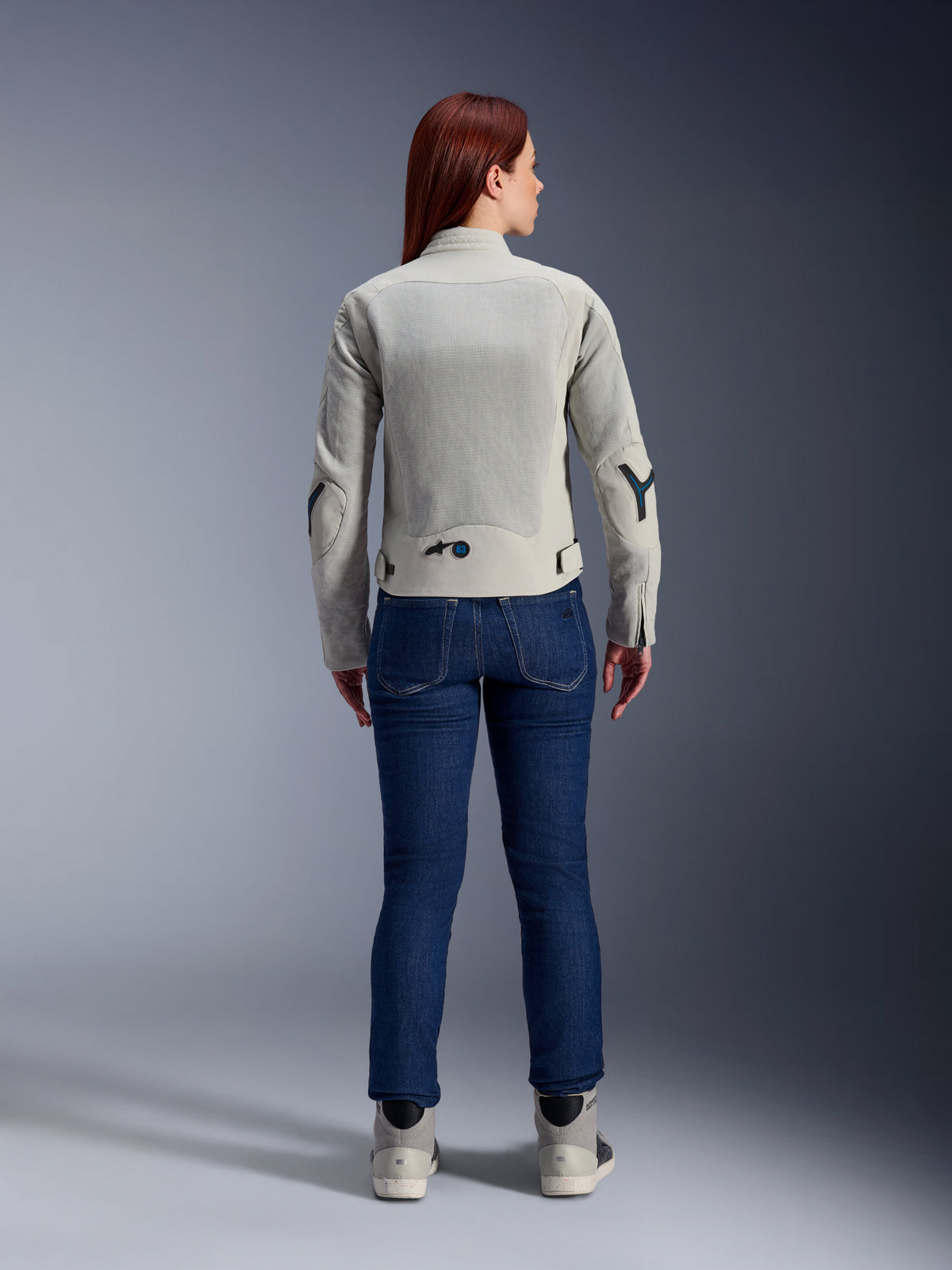 Alpinestars Stella Circal-1 Air Damenjacke in Metal Gray und Methyl Blue, Rückansicht, mit großen Mesh-Belüftungseinsätzen an Rücken und Armen, kombiniert mit dunkelblauen Jeans und grauen Motorradschuhen für einen modernen urbanen Motorrad-Look.