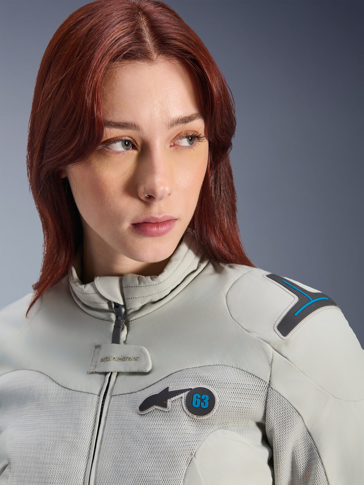 Frau in Alpinestars Stella Circal-1 Air Jacke, Textil-Motorradjacke für Damen, Metal Gray und Methyl Blue, Lifestyle-Nahaufnahme mit Mesh-Einsätzen zur Belüftung, gepolstertem Kragen und Alpinestars Logo-Patch mit der Nummer 63.