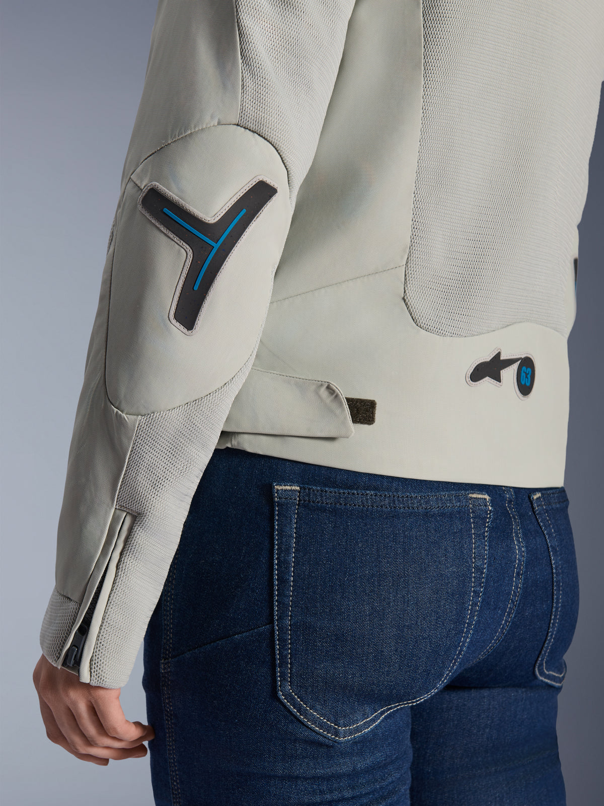 Alpinestars Stella Circal-1 Air Damenjacke in Metal Gray und Methyl Blue, Nahaufnahme der Rücken- und Ärmeldetails mit Mesh-Belüftungseinsätzen, neonblauen Akzenten an Ellbogen und Taille sowie verstellbarer Lasche, getragen mit dunkelblauen Denim-Jeans.