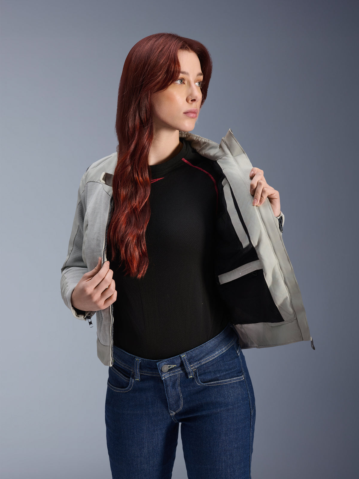 Alpinestars Stella Circal-1 Air Jacke in Metal Gray, weibliches Model öffnet die Jacke, um das interne Mesh-Futter und die Tasche zu zeigen, getragen mit blauen Jeans und einem schwarzen Oberteil, moderne urbane Motorradbekleidung.