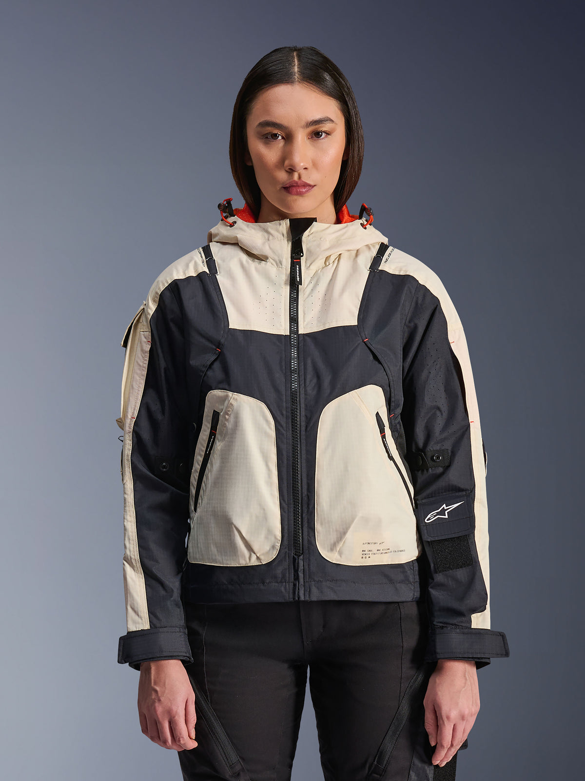 Alpinestars Molly Air Jacket, Women's Motorcycle Urban Jacket, Black Almond, front view on a model, featuring cream and black ripstop panels, hood with orange lining, front zipper closure, and large utility pockets, contemporary streetwear-inspired motorcycle gear