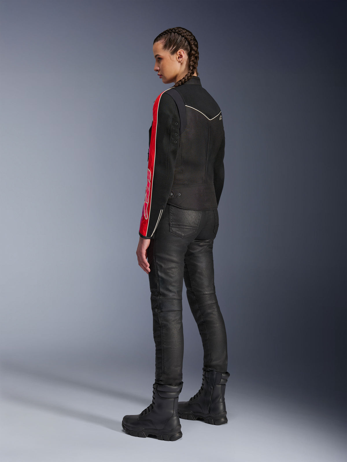 Woman wearing Alpinestars Stella T-Dyno Air Jacket in Black Bright Red Fuchsia, paired with black riding pants and black boots, side-profile view highlighting the red and fuchsia sleeve graphics and tailored biker fit.