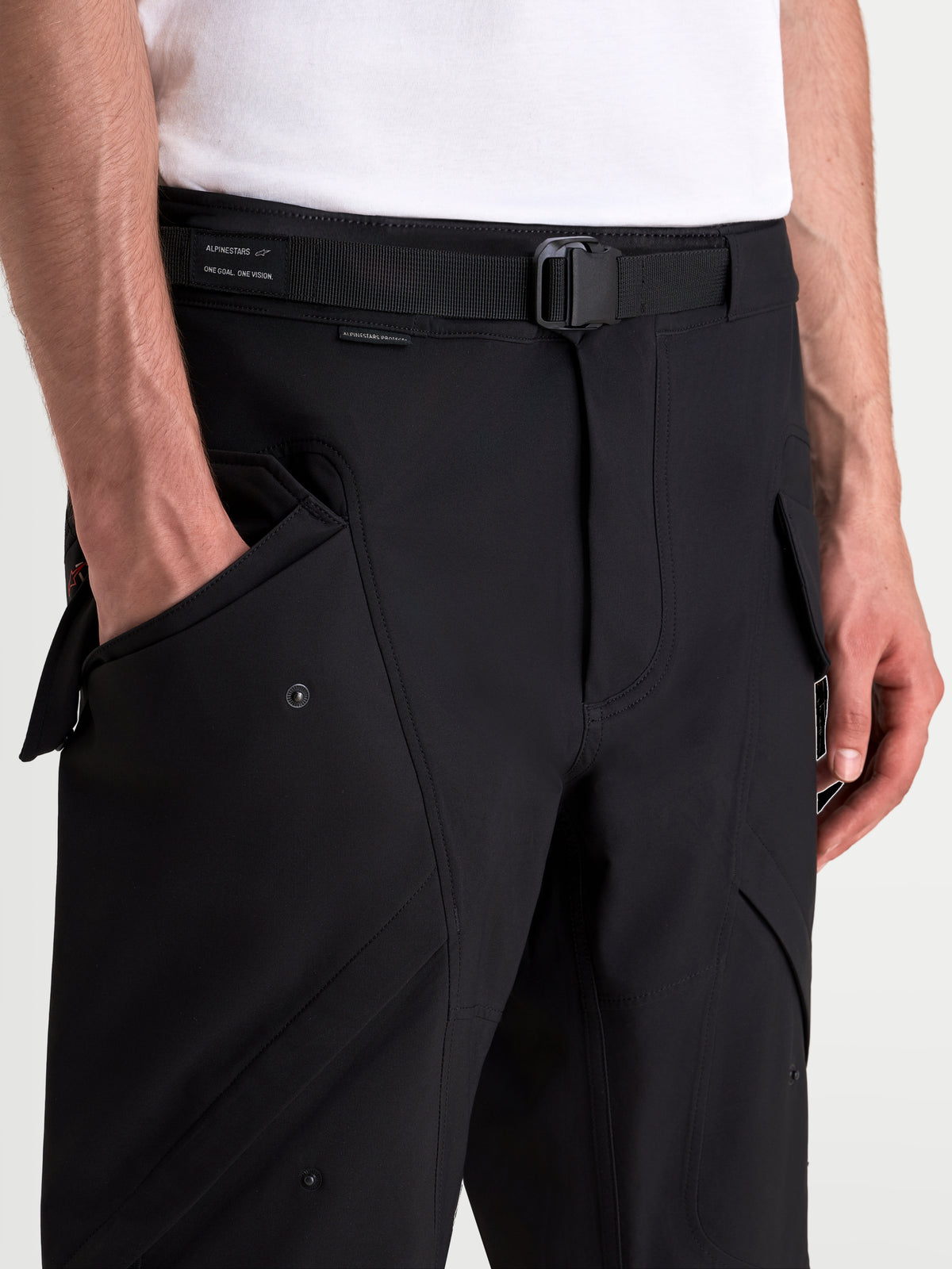 Alpinestars Juggernaut V 2 Drystar Hose, urbane Motorradhose in Schwarz, Nahaufnahme des verstellbaren Gürtels, der Magnetschnalle und der Vordertaschen an einem Model