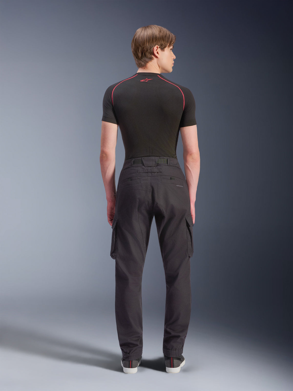 Alpinestars Flex-AST Cargo Hose - Short, Schwarz, urbane Motorradhose in der Rückansicht, mit seitlichen Cargotaschen und elastischen Säumen, getragen mit einem schwarzen kurzärmeligen Baselayer mit roten Kontrastnähten