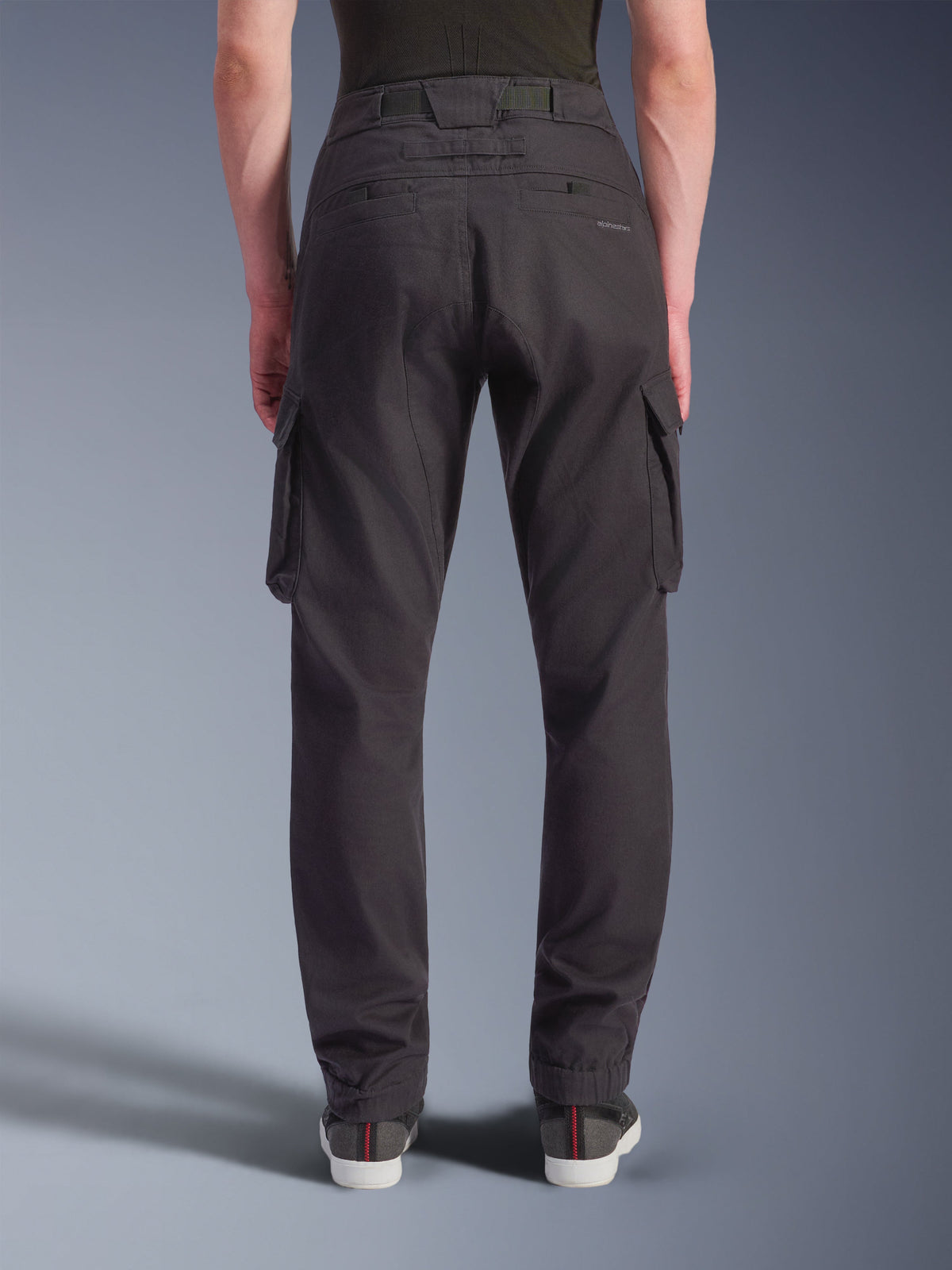 Alpinestars Flex-AST Cargo-Hose – Short, urbane Motorradhose, Schwarz, Rückansicht zeigt eine reguläre, konisch zulaufende Passform mit elastischen Säumen, große seitliche Cargotaschen und dezentes Branding auf der Gesäßtasche, getragen mit lässigen Sneakern