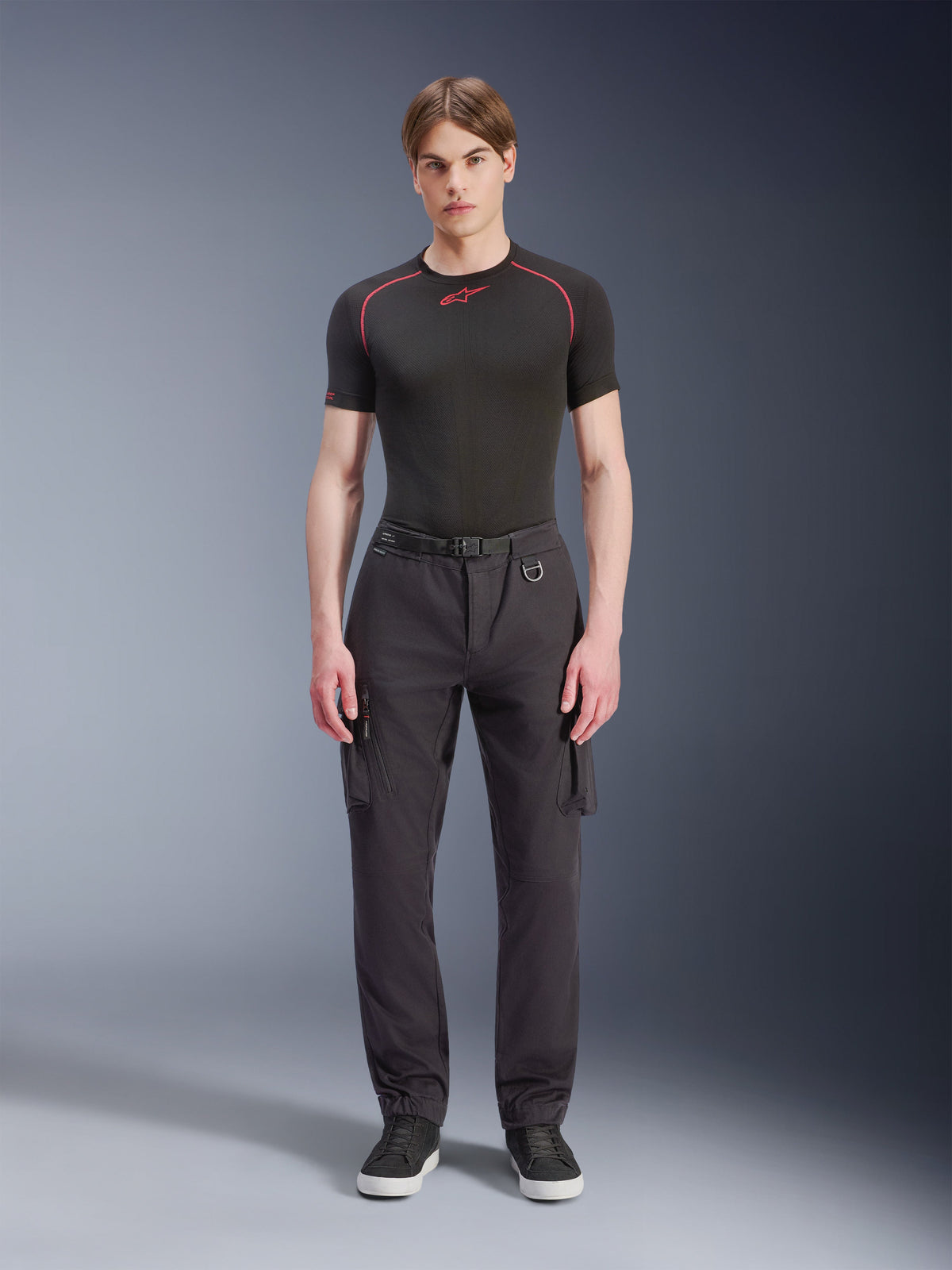 Alpinestars Flex-AST Cargo Hose – Kurz, Schwarz, getragen von einem männlichen Model mit schwarzem Performance-T-Shirt und schwarzen Sneakern, urbane Motorradhose mit mehreren Cargo-Taschen, konischer Passform und integriertem Gürtel mit Schnalle und D-Ring