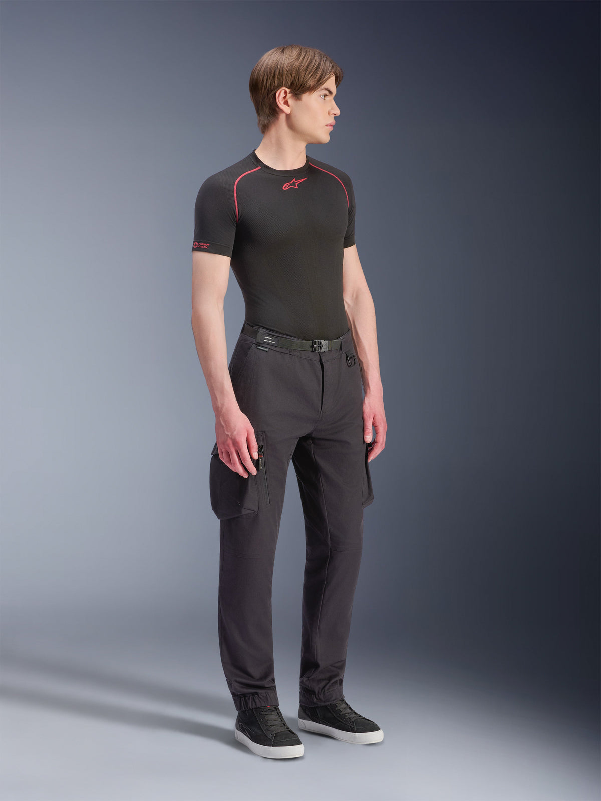 Männliches Model in Alpinestars Flex-AST Cargo Hose – Kurz in Schwarz, urbane Motorrad-Cargo-Hose mit Seitentaschen und schmal zulaufenden Beinen, kombiniert mit schwarzem Base-Layer und Sneakern, urbane Fahrbekleidung.