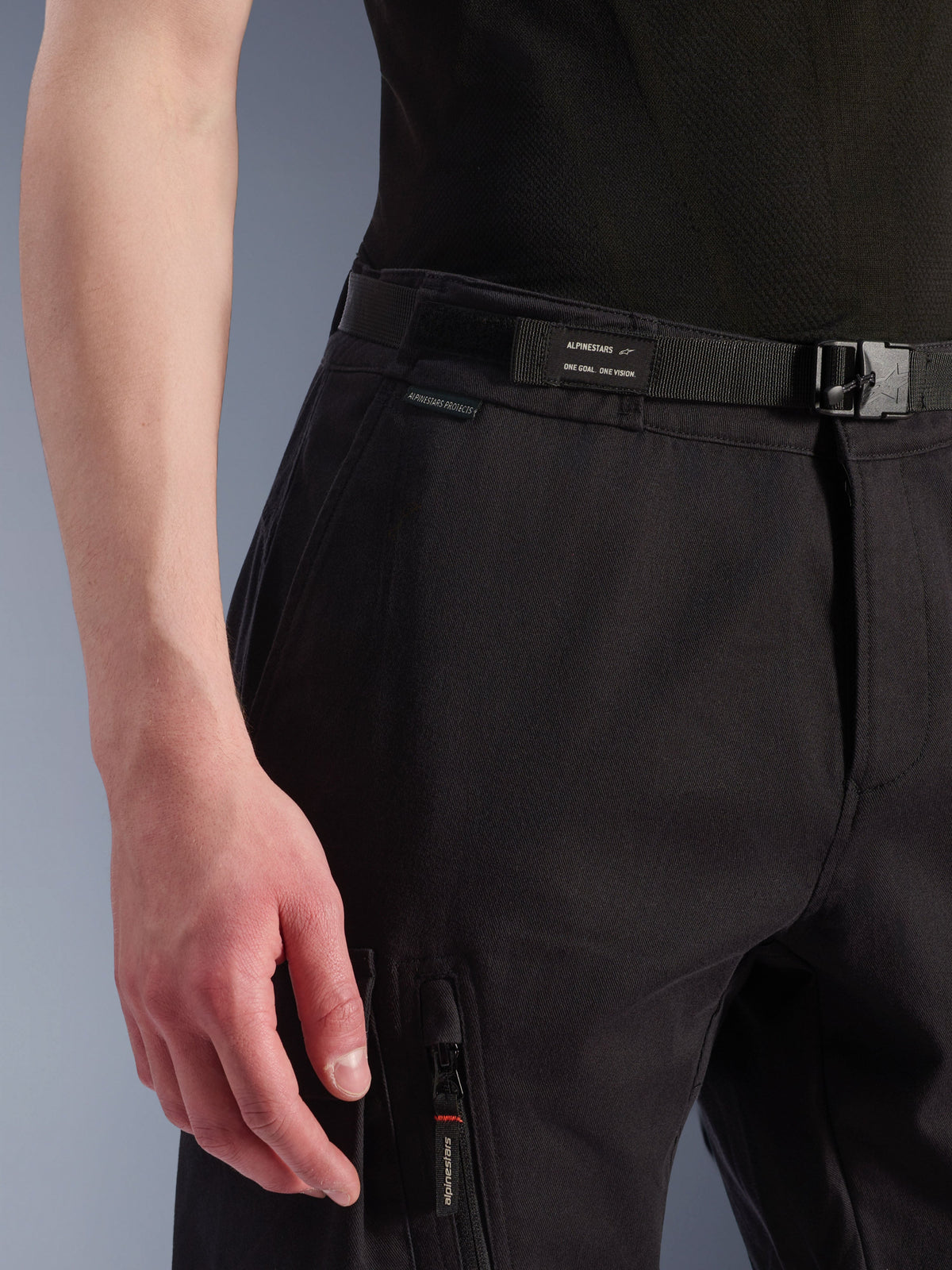 Alpinestars Flex-AST Cargo-Hose, Urbane Motorradhose, Schwarz, Nahaufnahme von Bund und Seitentasche, mit integriertem Gürtel mit Alpinestars-Branding, Schnallenverschluss und Reißverschlusstasche mit Marken-Logo am Schieber, technische Textilkonstruktion für urbane Fahrten