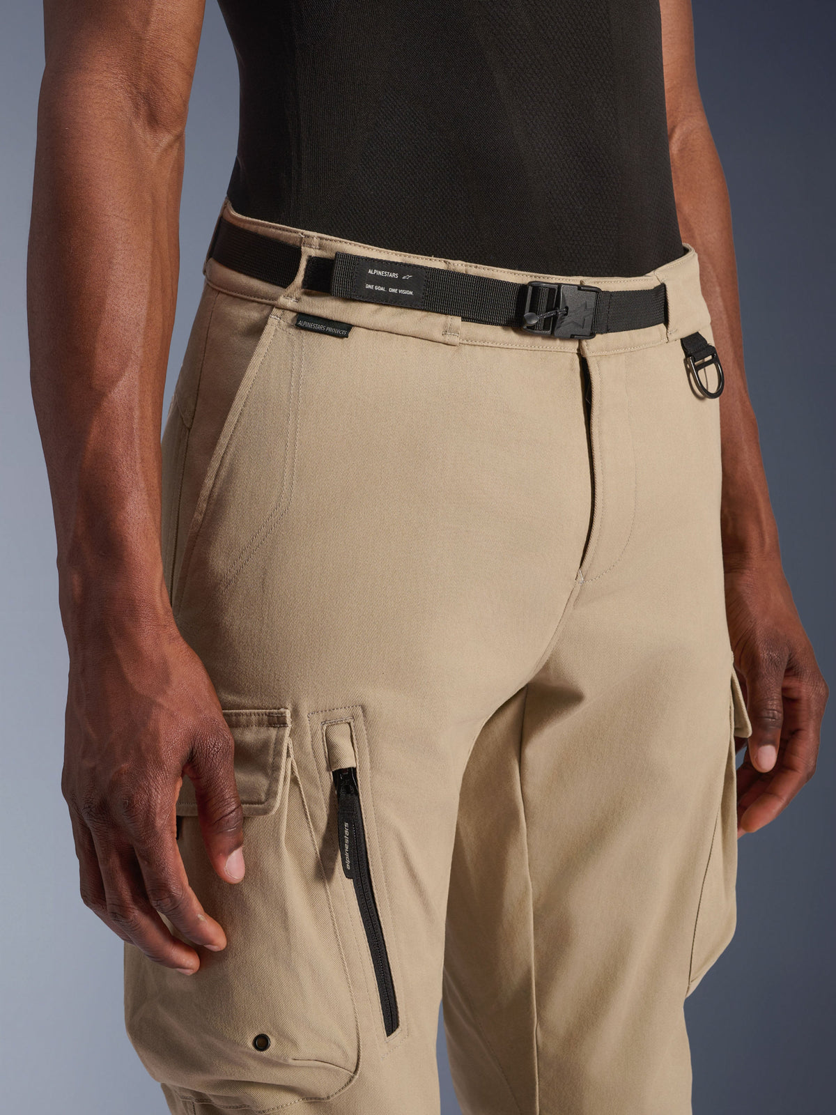 Alpinestars Flex-AST Cargo Pants - Short, Light Beige, close-up view of waist and thigh, featuring a black adjustable belt with Alpinestars branding, metal D-ring, and functional cargo pockets with zippers and snap flaps, urban contemporary motorcycle gear