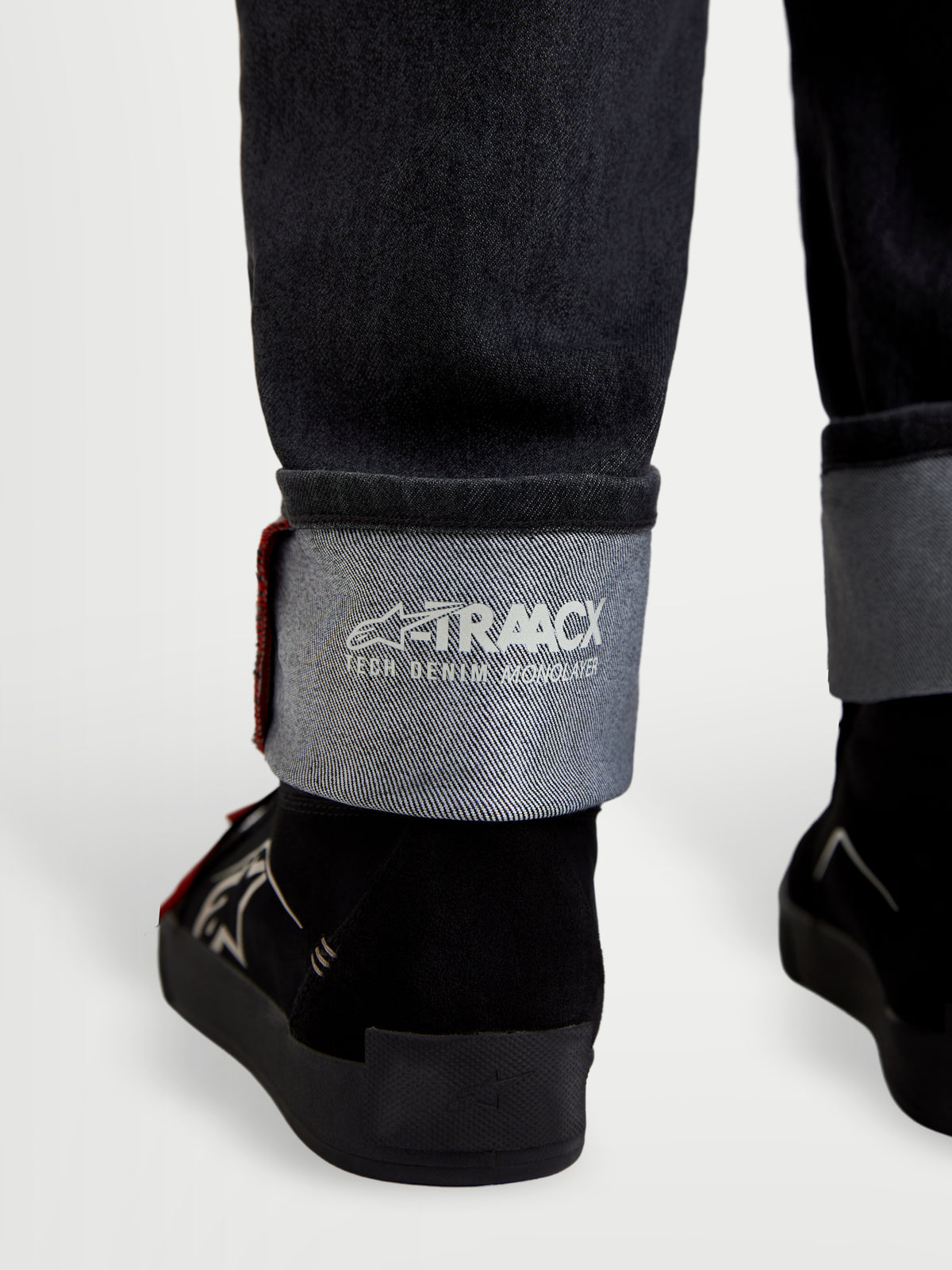 Alpinestars Flex Ast 7 Denim Hose, Motorrad-Jeans in verblasstem Schwarz, Nahaufnahme des umgeschlagenen Saums mit A-TRAACX Technical Denim-Branding und Selvedge-Details
