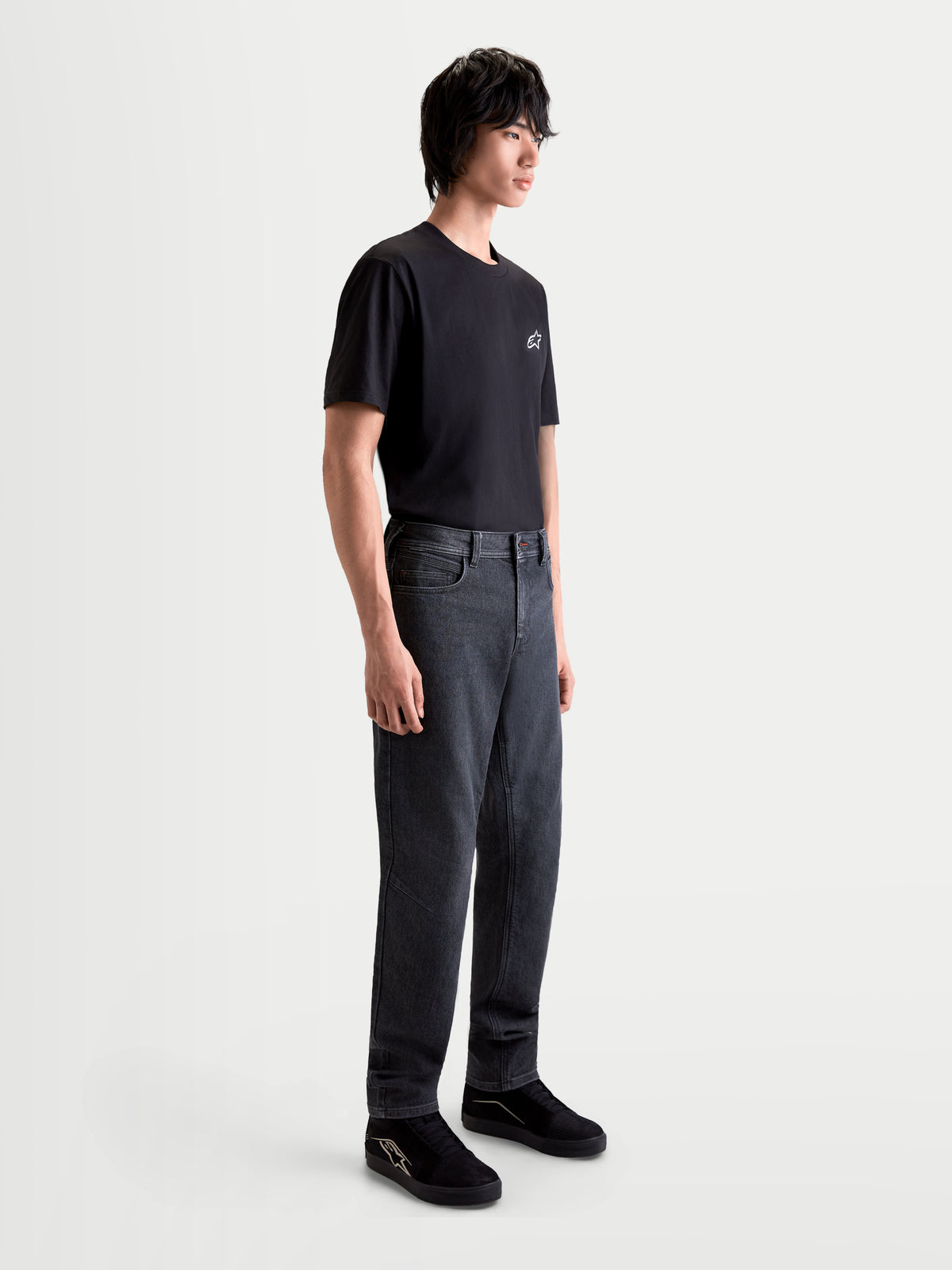 Alpinestars Flex Ast 7 Denim Hose, urbane Herren-Motorradjeans in verblasstem Schwarz, Seitenprofil an einem Model in schwarzem T-Shirt und Schuhen, AA-zertifizierte einlagige technische Jeanskonstruktion