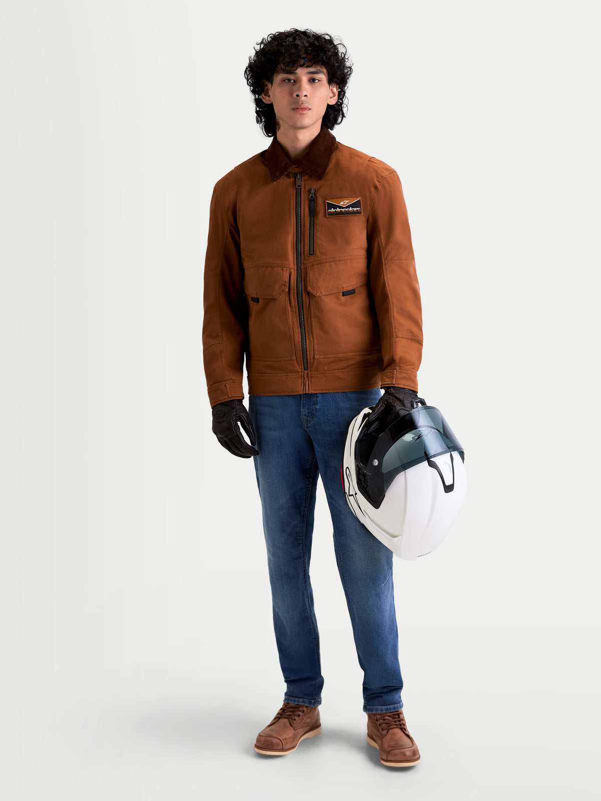Alpinestars Flex Ast 7 Denim Hose, Herren-Urban-Motorradjeans in Hellblau, getragen von einem Model, das einen Helm und eine passende Jacke hält