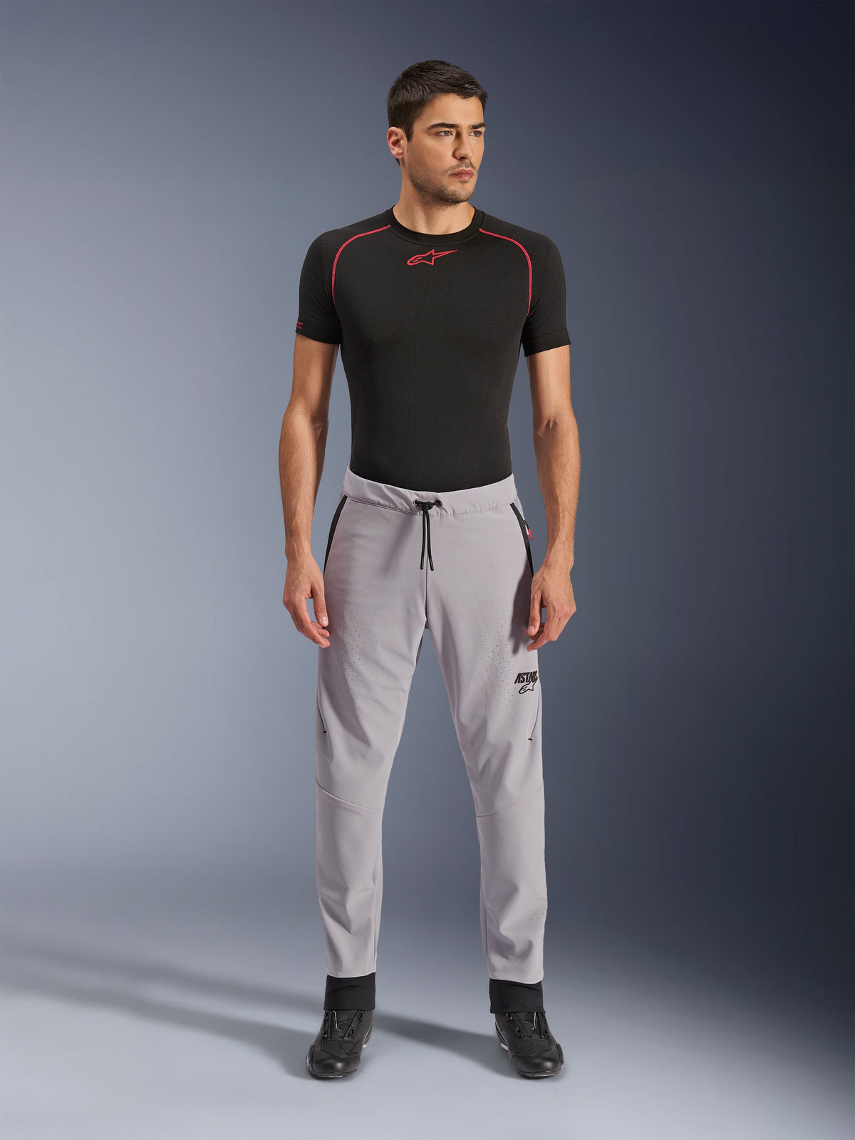 Alpinestars Aeroshell Airflow Hose, Mittelgrau, leichte Textilhose mit laserperforierten Belüftungszonen und Kordelzug am Bund, getragen von einem Modell mit schwarzem Kompressionsshirt und schwarzen Motorradstiefeln, cleanes und modernes Sport-Riding-Design