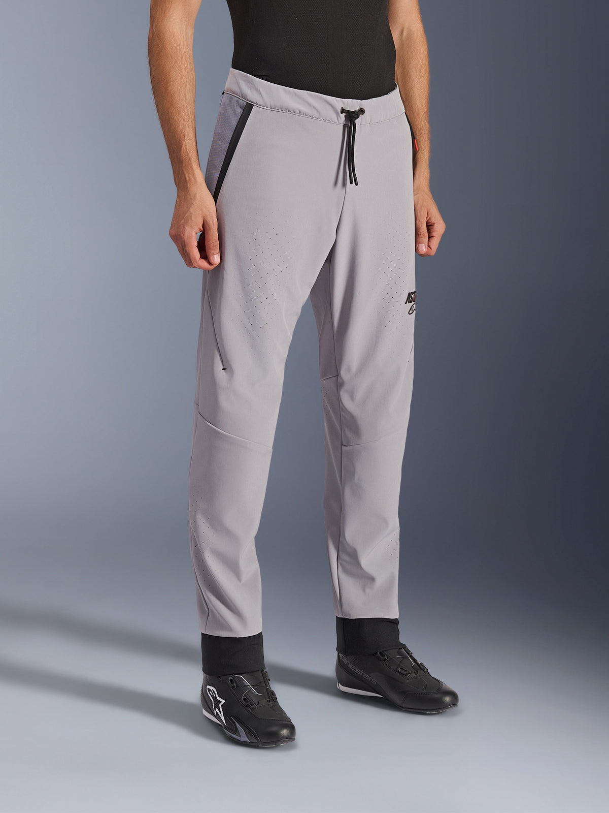Alpinestars Aeroshell Airflow Hose, Mittelgrau, leichte Motorradhose mit laserperforierten Belüftungszonen an Oberschenkeln und Schienbeinen, elastischer Bund mit Kordelzug und schmale sportliche Passform, präsentiert an einem Modell mit schwarzen Motorradschuhen.