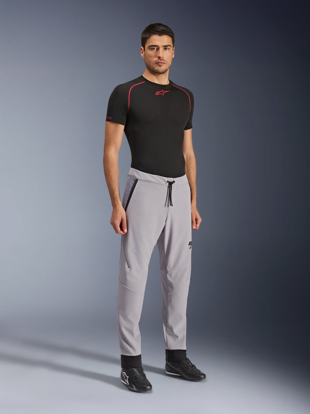 Alpinestars Aeroshell Airflow Hose, Motorradhose, Mittelgrau, getragen von einem Modell mit schwarzem technischen T-Shirt und schwarzen Motorradschuhen, mit laserperforierten Belüftungszonen, elastischem Bund mit Kordelzug und sportlicher Passform.