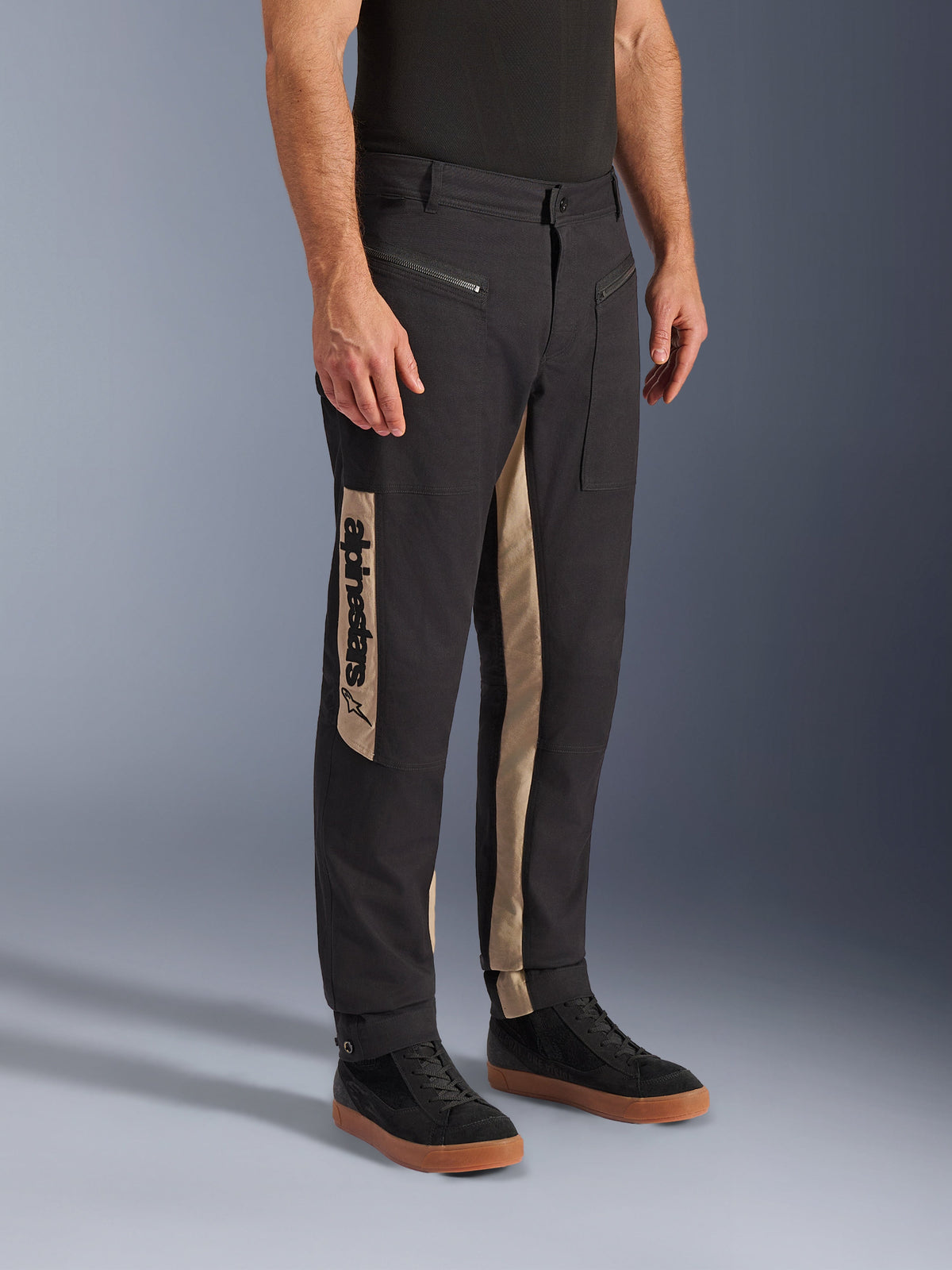 Alpinestars Flex-AST Canvas Pants, Urban Motorcycle Pants, Black Aluminum, featuring tan side panels with a vertical Alpinestars logo, workwear-inspired design with zippered pockets and ergonomic cut, worn with casual black sneakers for a modern city look.