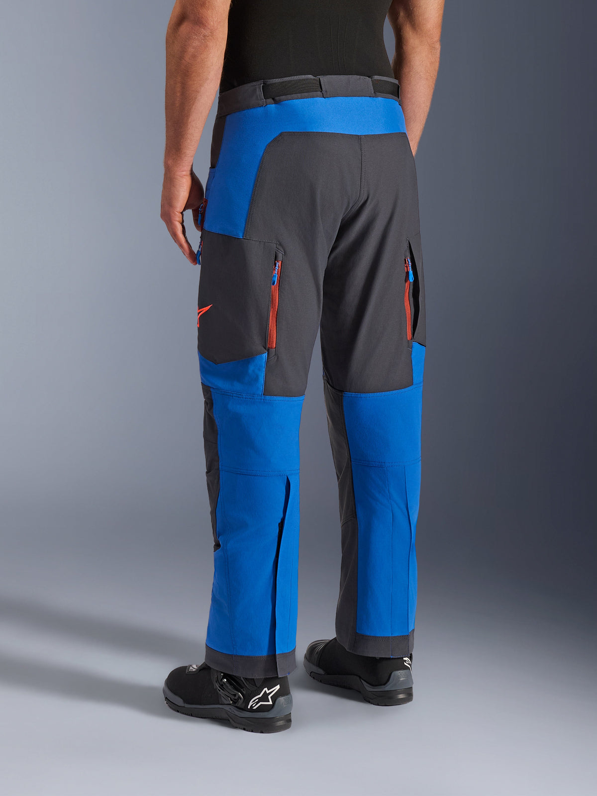 Alpinestars Maxdura Dual Hose, Königsblau und Dunkelgrau, Rückansicht mit Reißverschlusstaschen und Belüftungszonen, Überstiefel-Passform getragen mit schwarzen Alpinestars Stiefeln, strapazierfähige Adventure- und Dual-Sport-Ausrüstung