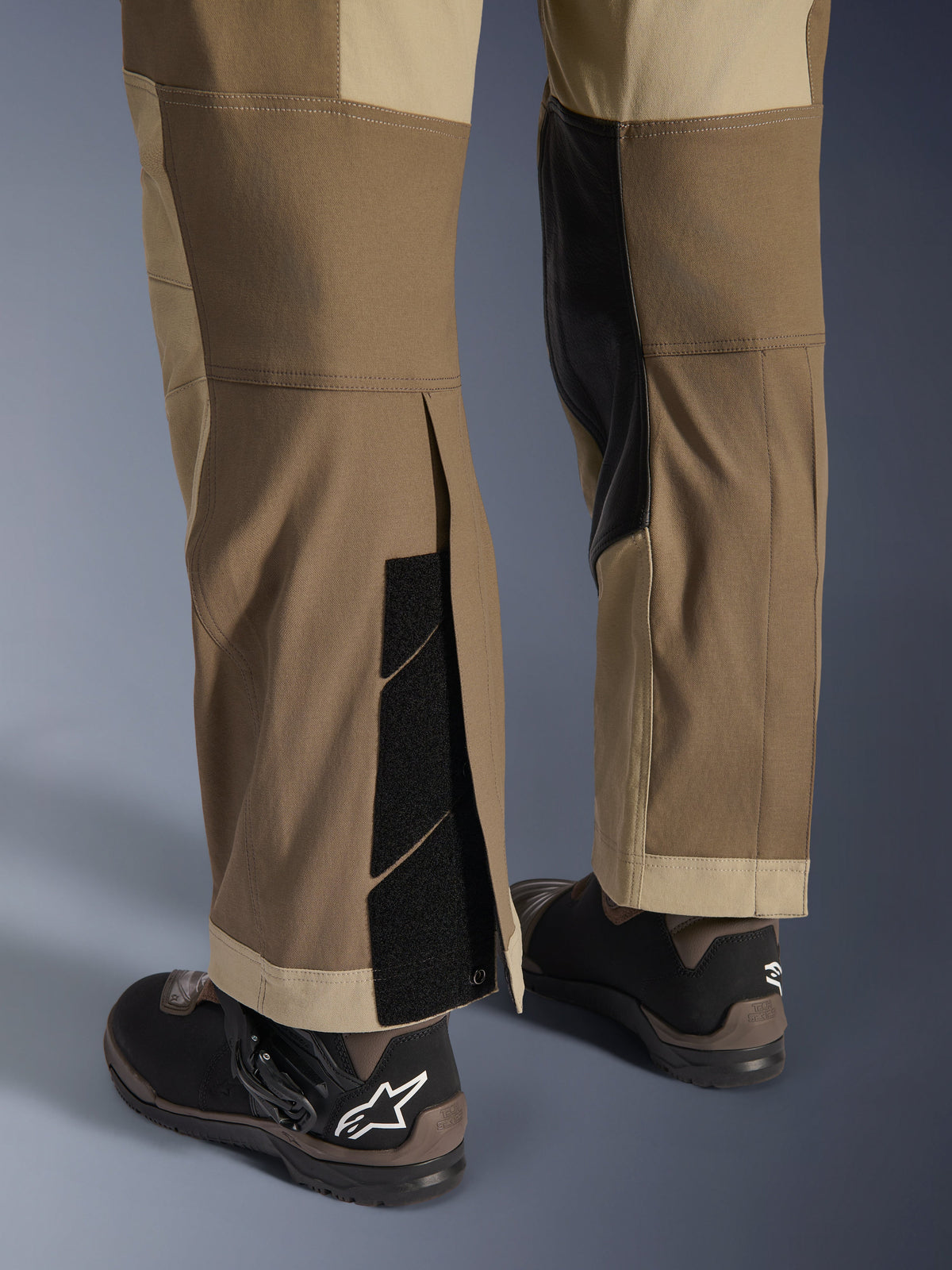 Alpinestars Maxdura Dual Hose in Walnut Aluminum, Detailansicht von Unterschenkel und Saum mit Über-den-Stiefel-Design, verstellbare Klettverschlüsse und verstärkte Innenpaneele, kombiniert mit schwarzen Motorradstiefeln.