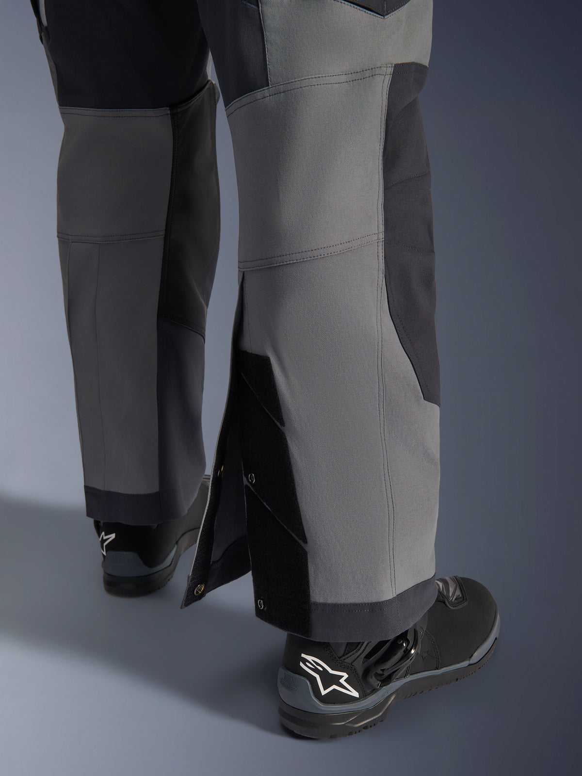 Alpinestars Maxdura Dual Hose, Adventure-Motorradhose, Dunkelgrau und Deep Gray, Nahaufnahme des verstellbaren Over-the-Boot-Beinsaums mit Druckknopfverschlüssen und verstärkten Einsätzen, getragen mit schwarzen Alpinestars Stiefeln, robustes technisches Design für Dual-Sport-Fahrten