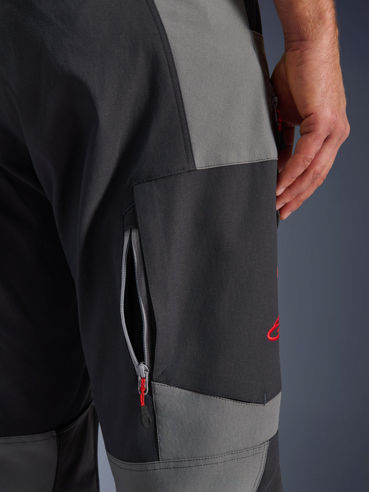 Alpinestars Maxdura Dual Hose, Adventure-Motorradhose in Dunkelgrau und Deep Gray, Nahaufnahme des Oberschenkels mit Reißverschluss-Belüftungsöffnung und rotem gesticktem Logo, strapazierfähige Stretch-Polyamid-Konstruktion