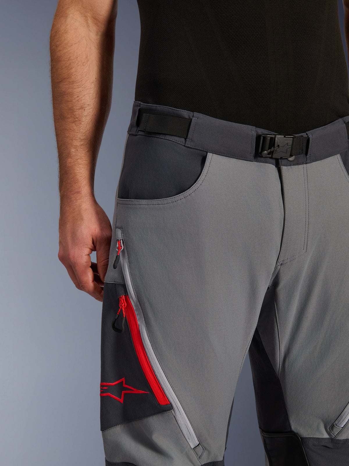 Alpinestars Maxdura Dual Hose, Adventure-Motorradhose, Dunkelgrau und Tiefgrau, Nahaufnahme mit verstellbarem Taillengürtel mit Magnetschnalle, Cargotasche mit Reißverschluss, roten Details und Alpinestars-Logo.