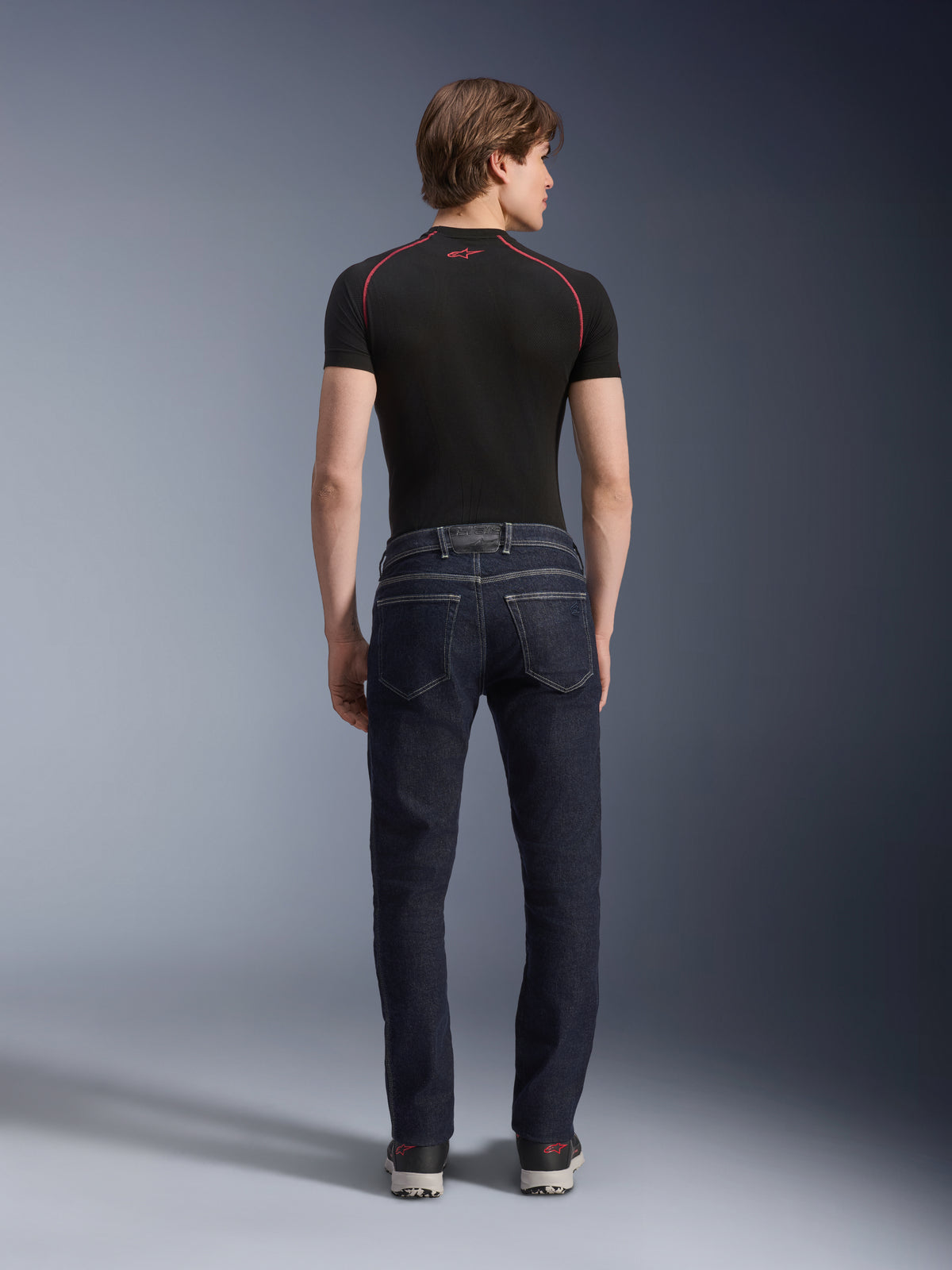 Alpinestars Copper V3 Denim Hose in Rinse Blue, urbane Motorradjeans in der Rückansicht, Regular Fit mit geradem Bein und Gesäßtaschen, getragen mit einem schwarzen Kurzarm-Oberteil und Sneakern.