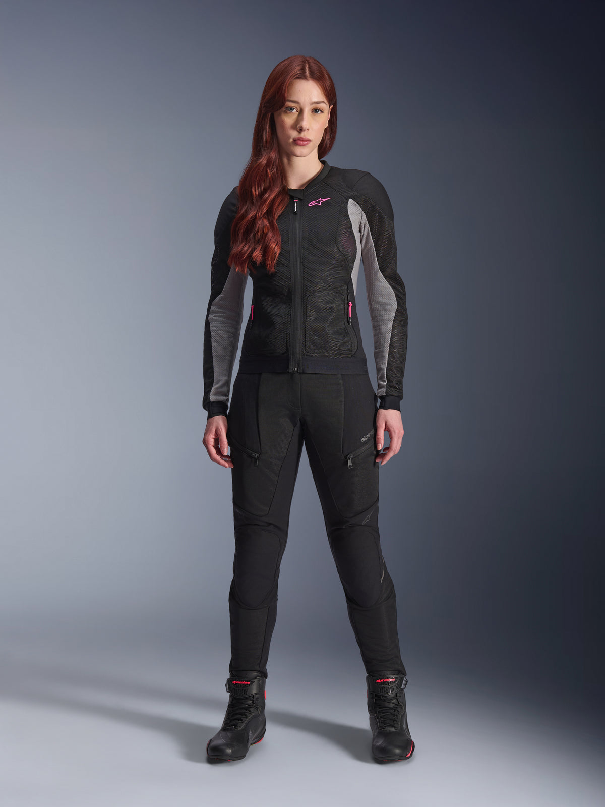 Alpinestars Stella Troop-Air Hose, Damen-Motorradhose in Schwarz, mit Mesh-Einsätzen und Reißverschlusstaschen, kombiniert mit einer passenden schwarz-grauen Mesh-Jacke mit pinken Akzenten und schwarzen Motorradstiefeln, komplettes urbanes Motorrad-Outfit.