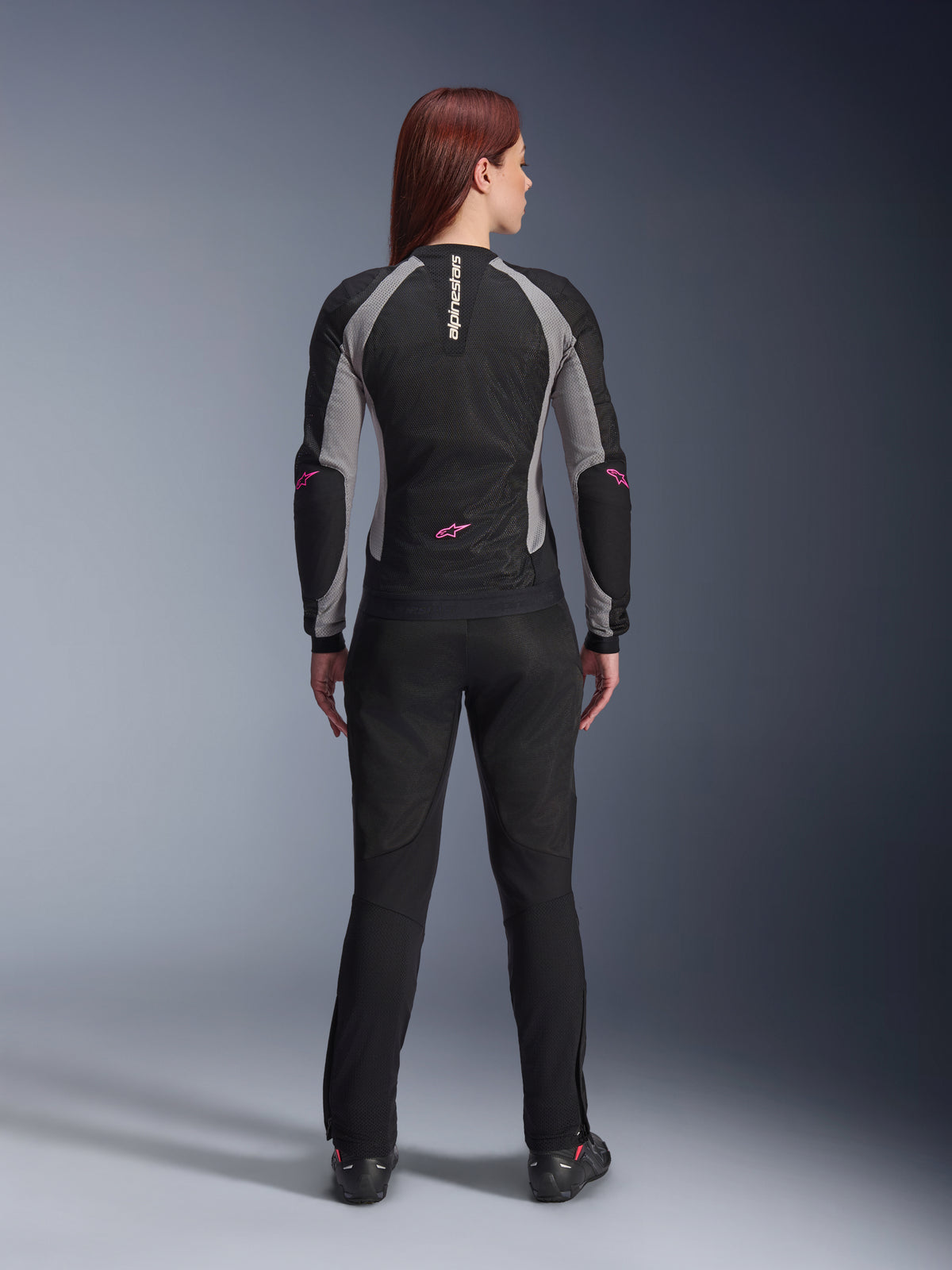 Stella Troop-Air Damenjacke und passende Hose in der Rückansicht, Schwarz, Ash Gray und Pink Fluo, leichte Mesh-Motorradausrüstung mit grauen Einsätzen und pinkfarbenen Fluo-Akzenten, mit vertikalem Alpinestars-Branding und Stern-Logos.