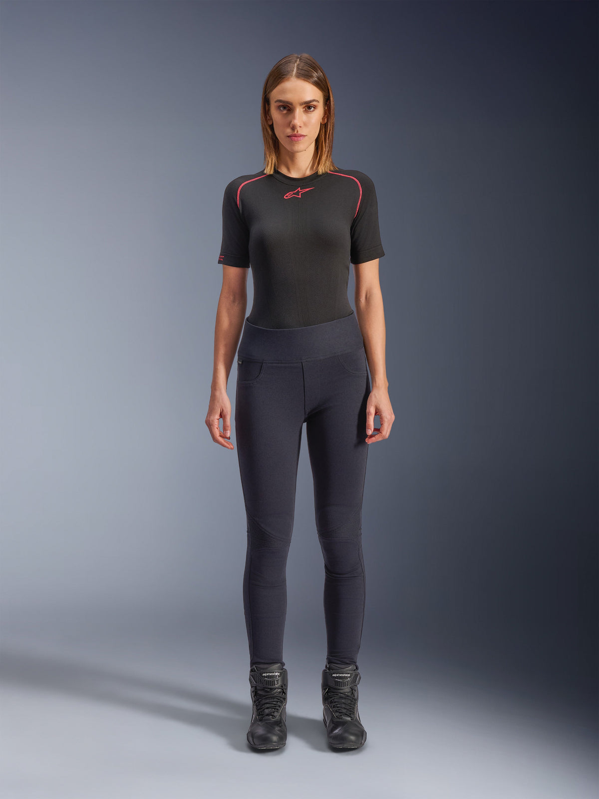 Alpinestars Stella Flex-AST Leggings, urbane Damen-Motorrad-Leggings in Schwarz, schmal geschnittenes High-Waist-Design, getragen mit einem schwarzen, kurzärmeligen Funktions-Oberteil und schwarzen Motorradstiefeln, mit Akkordeon-Kniepaneelen und einem modernen, minimalistischen Look.