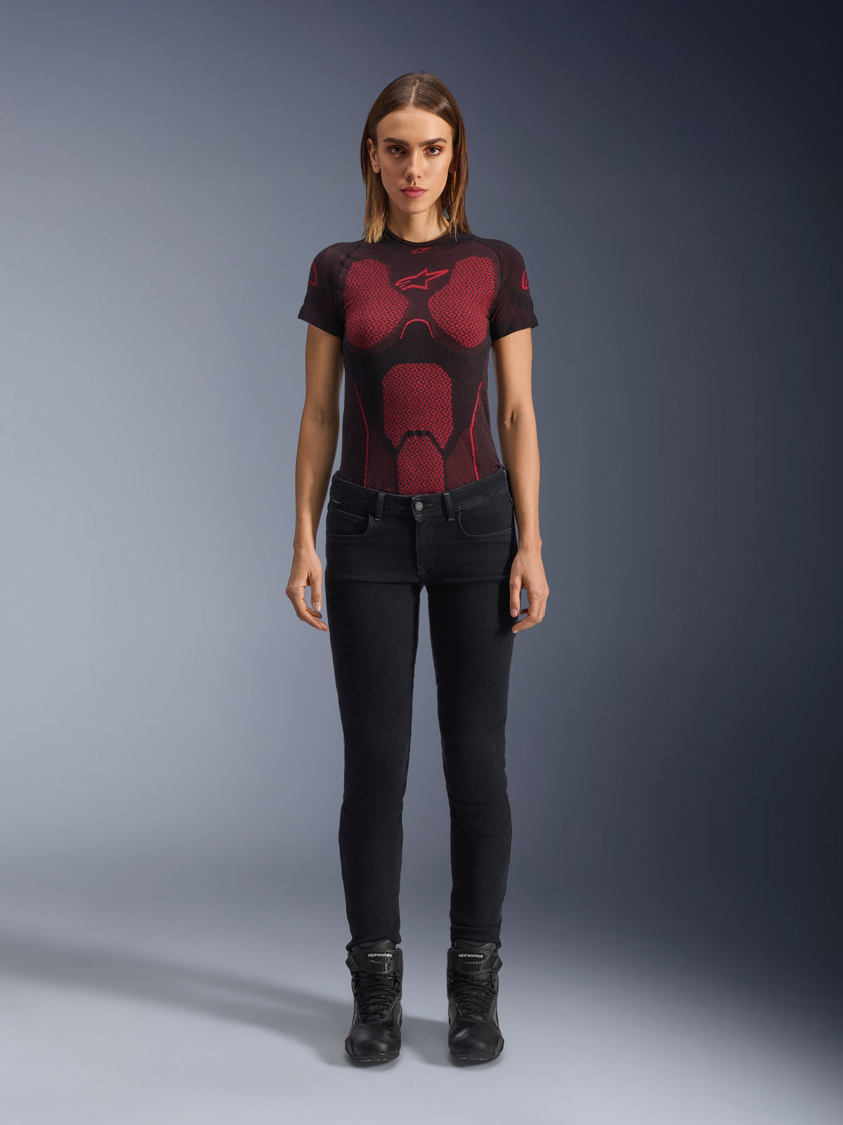 Alpinestars Daisy V3 Damen-Motorradjeans, Rinse Black, Slim-Fit Motorradhose, getragen von einem Model mit einem rot-schwarz gemusterten technischen T-Shirt und schwarzen Motorradstiefeln, lässige urbane Fahrausrüstung mit femininer Silhouette und High-Waist-Design.